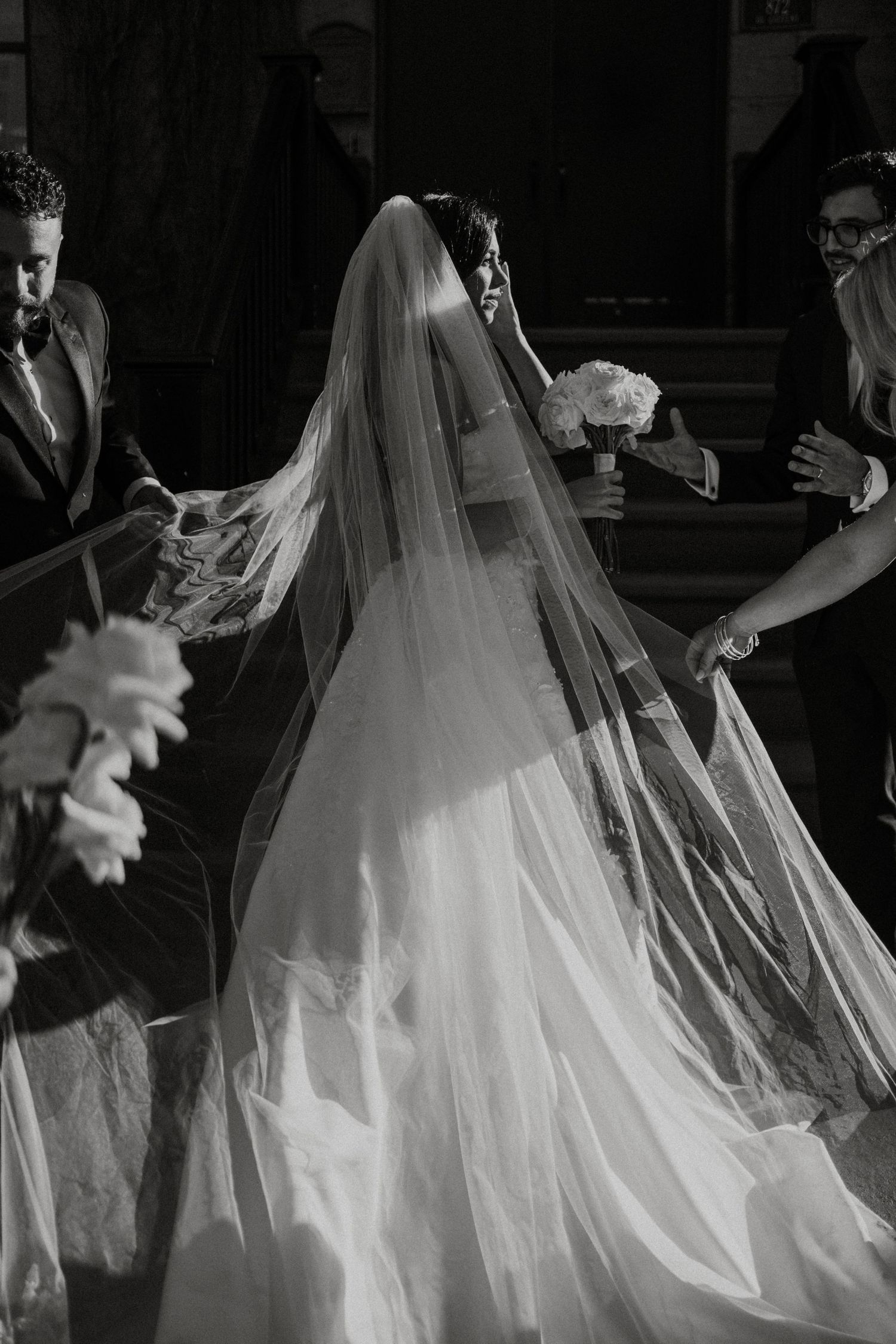 Black and white photo of a bride's flowing veil trailing behind her wedding dress during the ceremony.