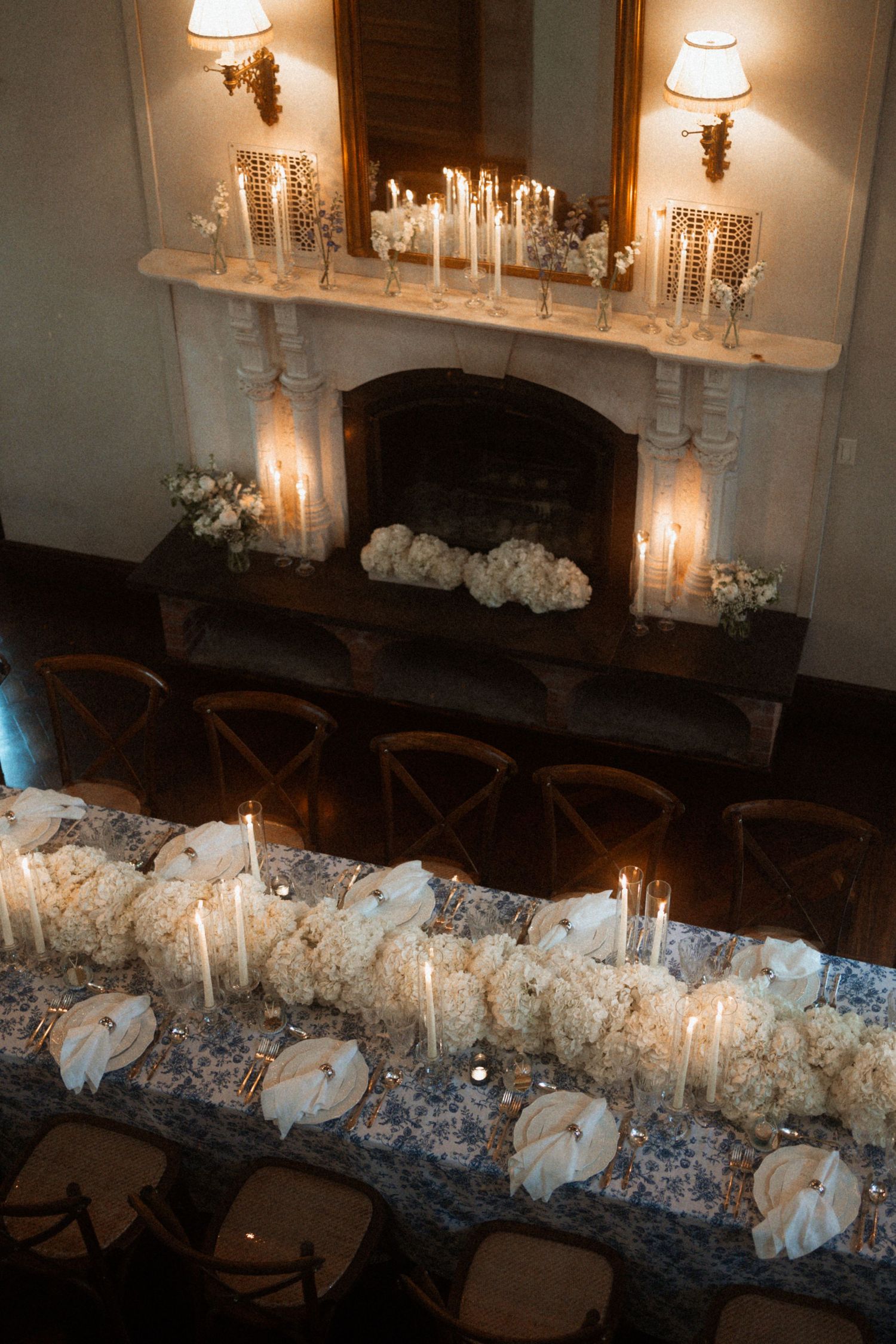 Long dining table decorated with an elegant white floral centerpiece and glowing candelabras in a dimly lit room.