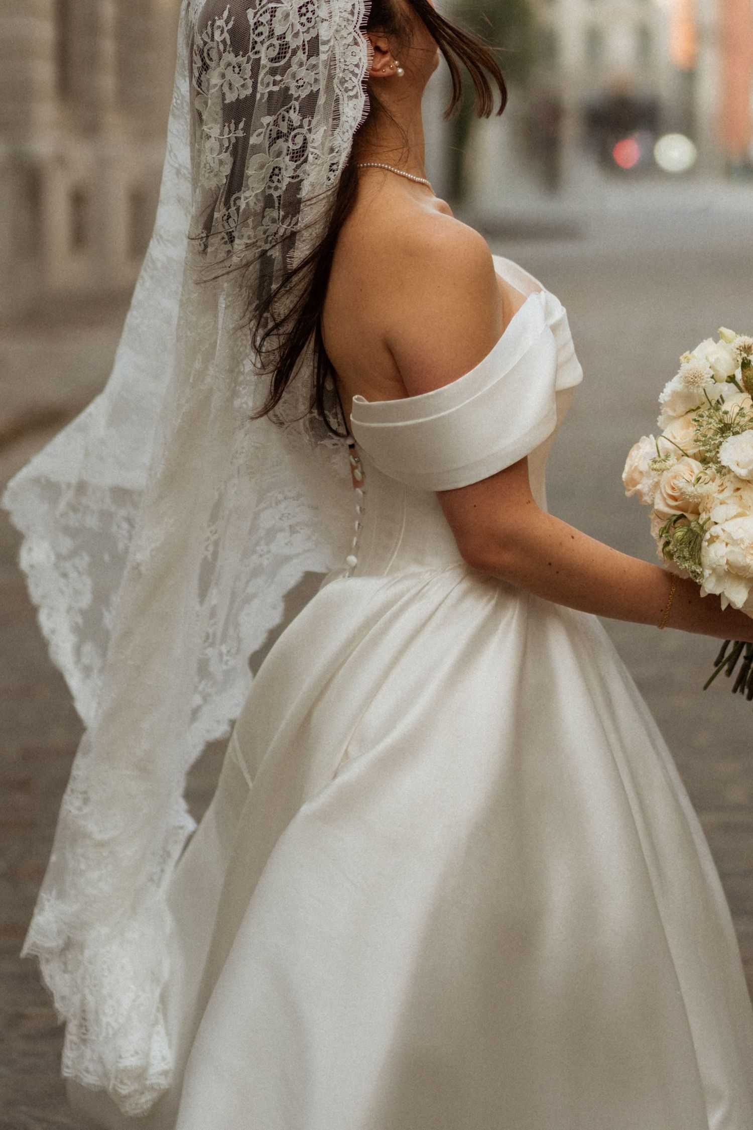 Close-up view of a bride in an off-shoulder ball gown wedding dress with lace veil and white bouquet.