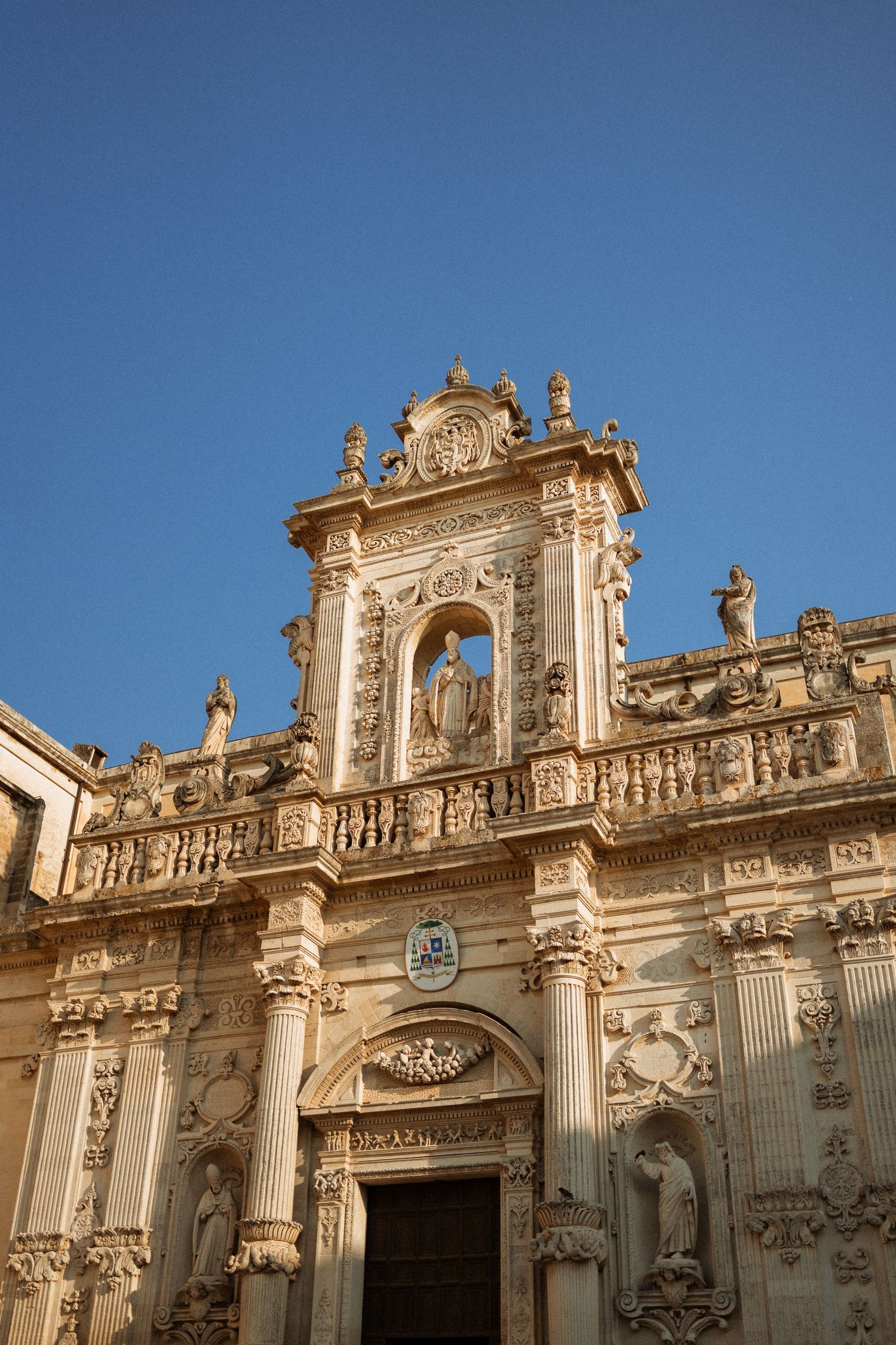 Ornate baroque facade of a historic cathedral with detailed stone carvings and columns against a bright blue sky.