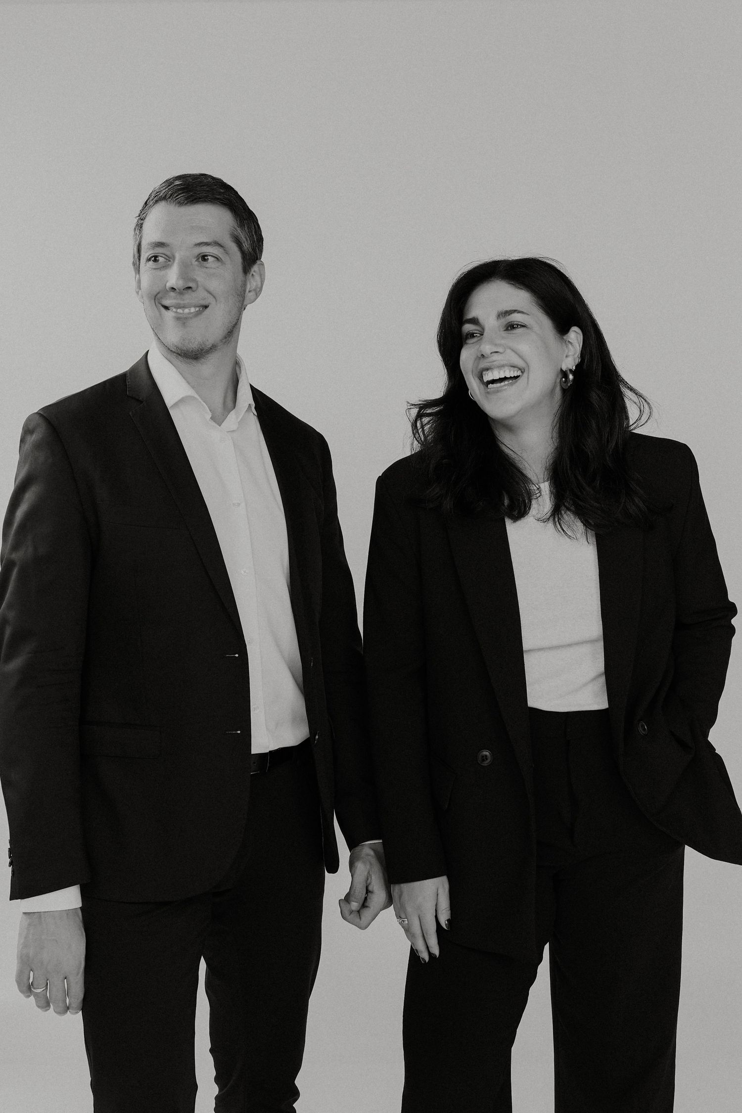 A black and white photo shows people in formal attire laughing and holding hands in a candid group pose.
