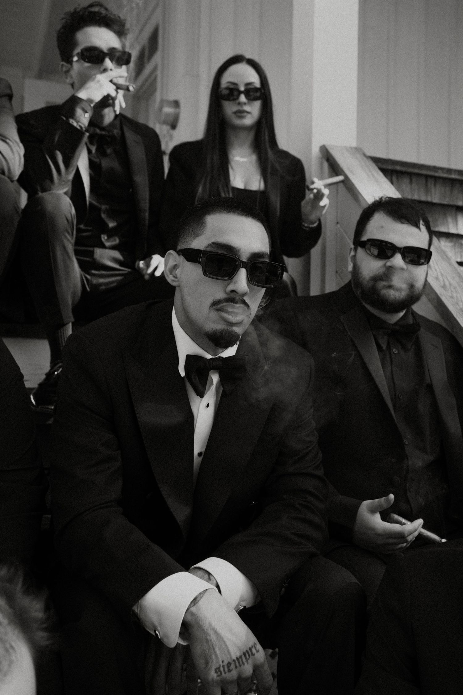 A group of people wearing black suits and sunglasses sit together in a formal setting.