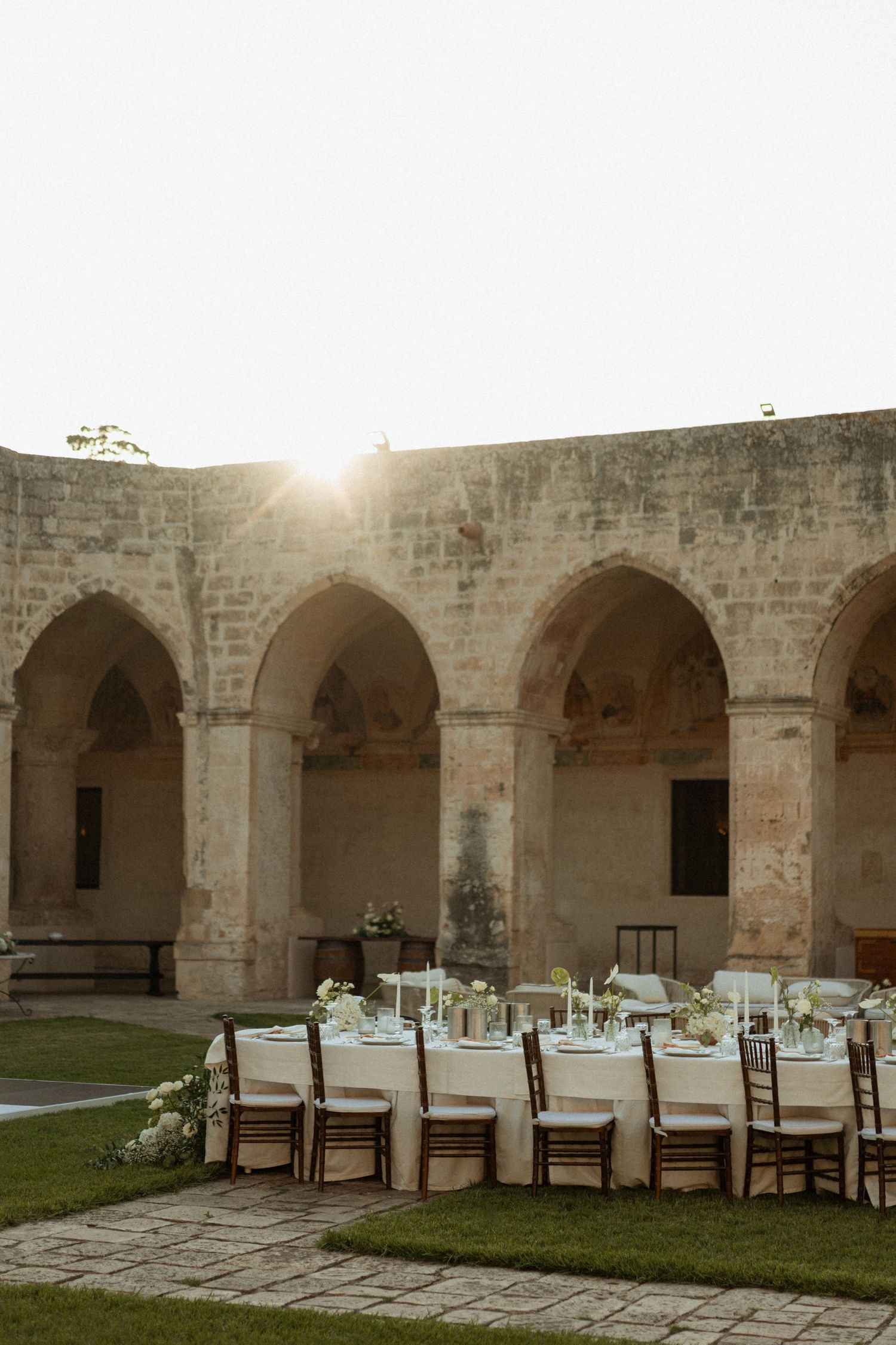Elegant outdoor wedding reception set in a historic stone courtyard with arched columns and sunlit ambiance.