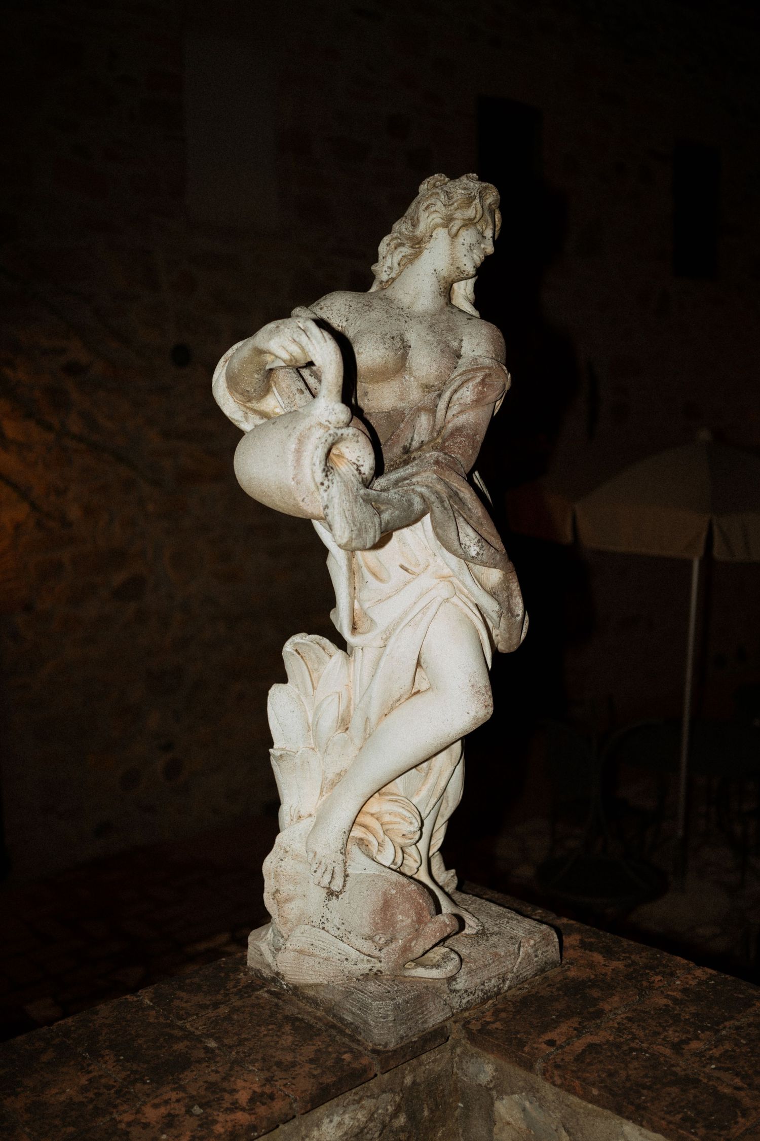 Ancient marble statue of a female figure pouring water from an urn, displayed in a dimly lit stone interior.