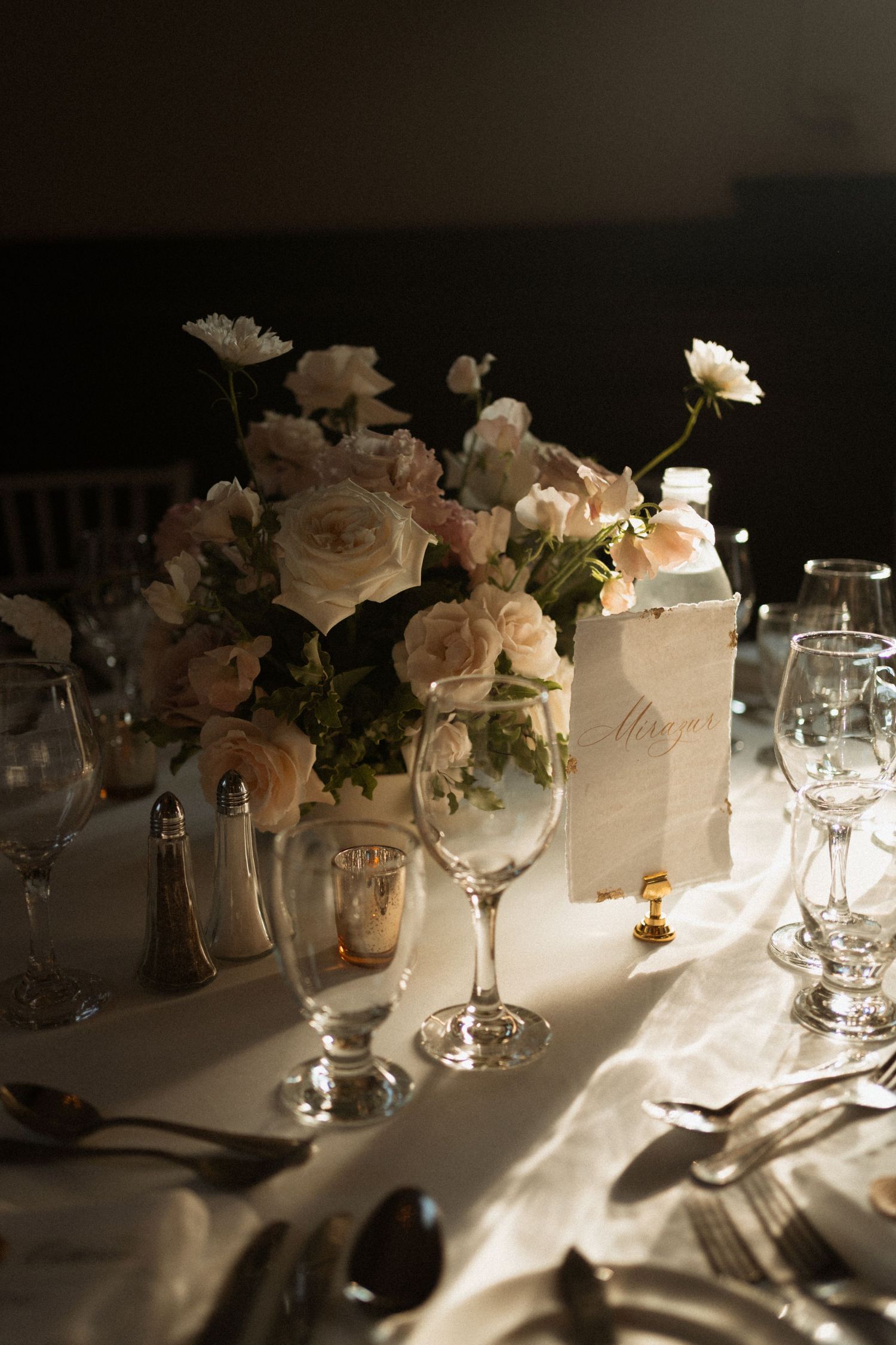 Elegant wedding reception table setting with blush roses, crystal glasses, and soft candlelight.