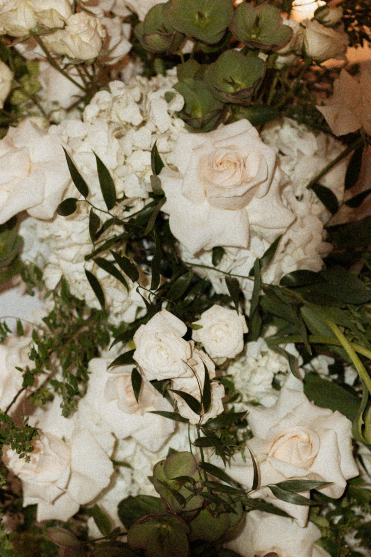 Elegant arrangement of cream-colored roses and mixed white flowers with lush green foliage creates a romantic wedding bouquet.