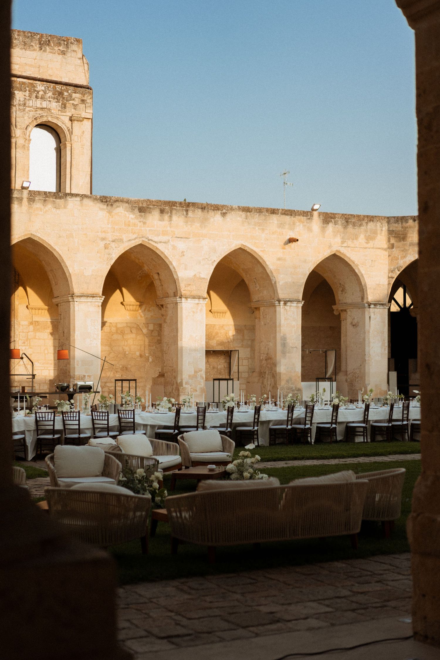 Elegant arched colonnade with tables and chairs set up for dining at a historic Mediterranean-style venue at sunset.