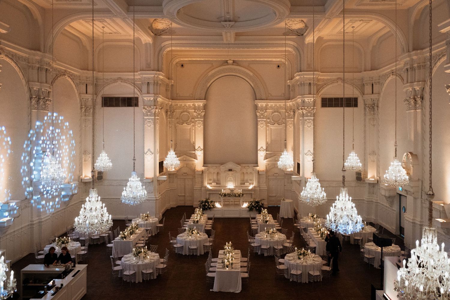 Elegant ballroom with ornate crystal chandeliers and white decor creates a luxurious atmosphere for special events.
