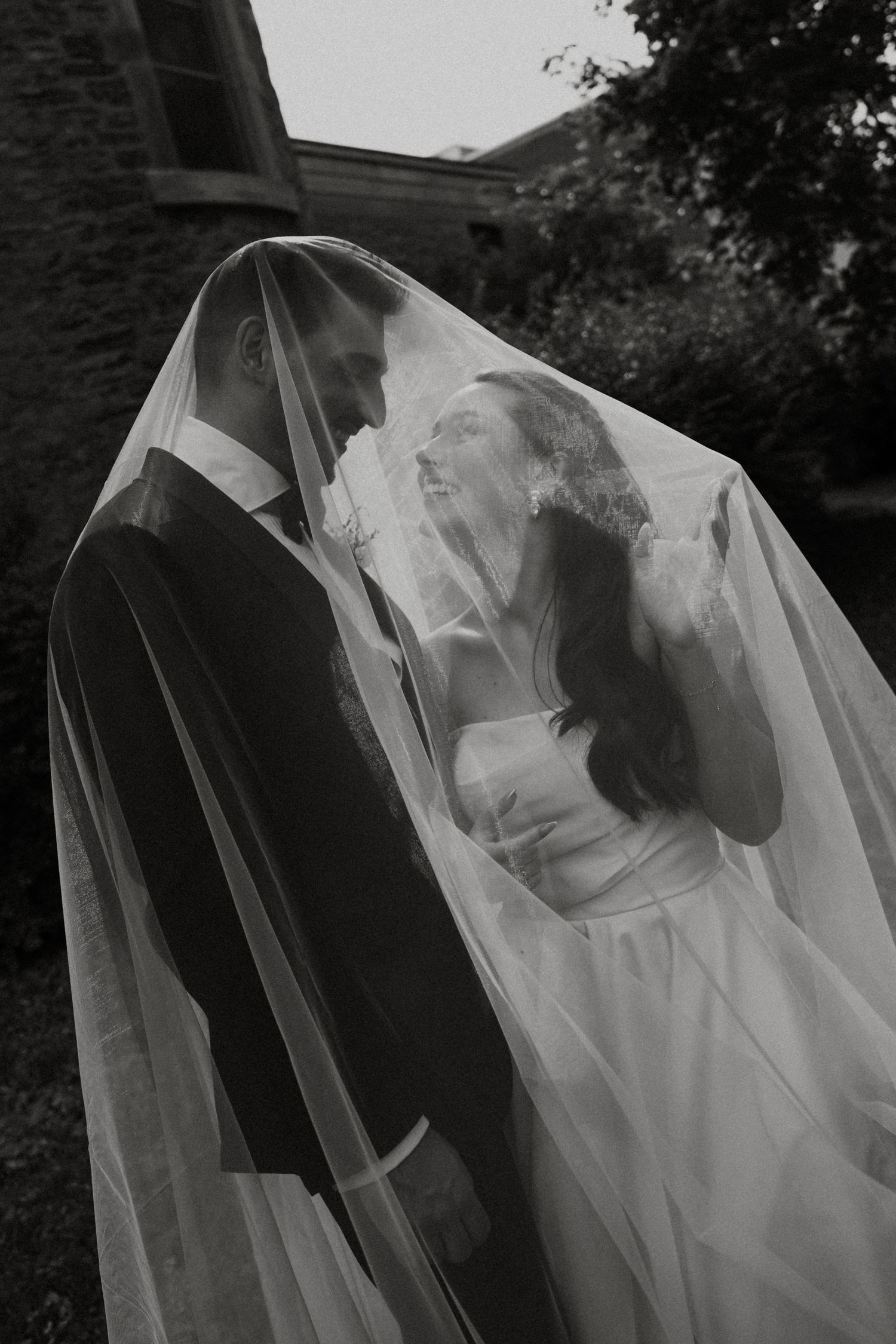 Artistic black and white photo of flowing wedding veil in natural outdoor setting.