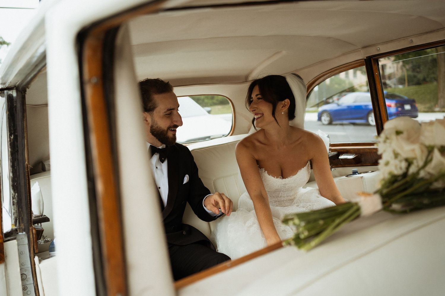 Bride and groom share a joyful moment seated together in a classic vintage wedding car.
