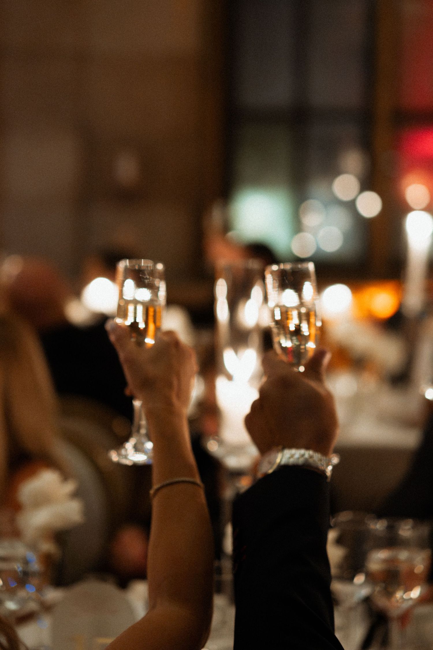 People raise champagne glasses in a toast during an elegant dinner celebration with soft bokeh lighting in the background.