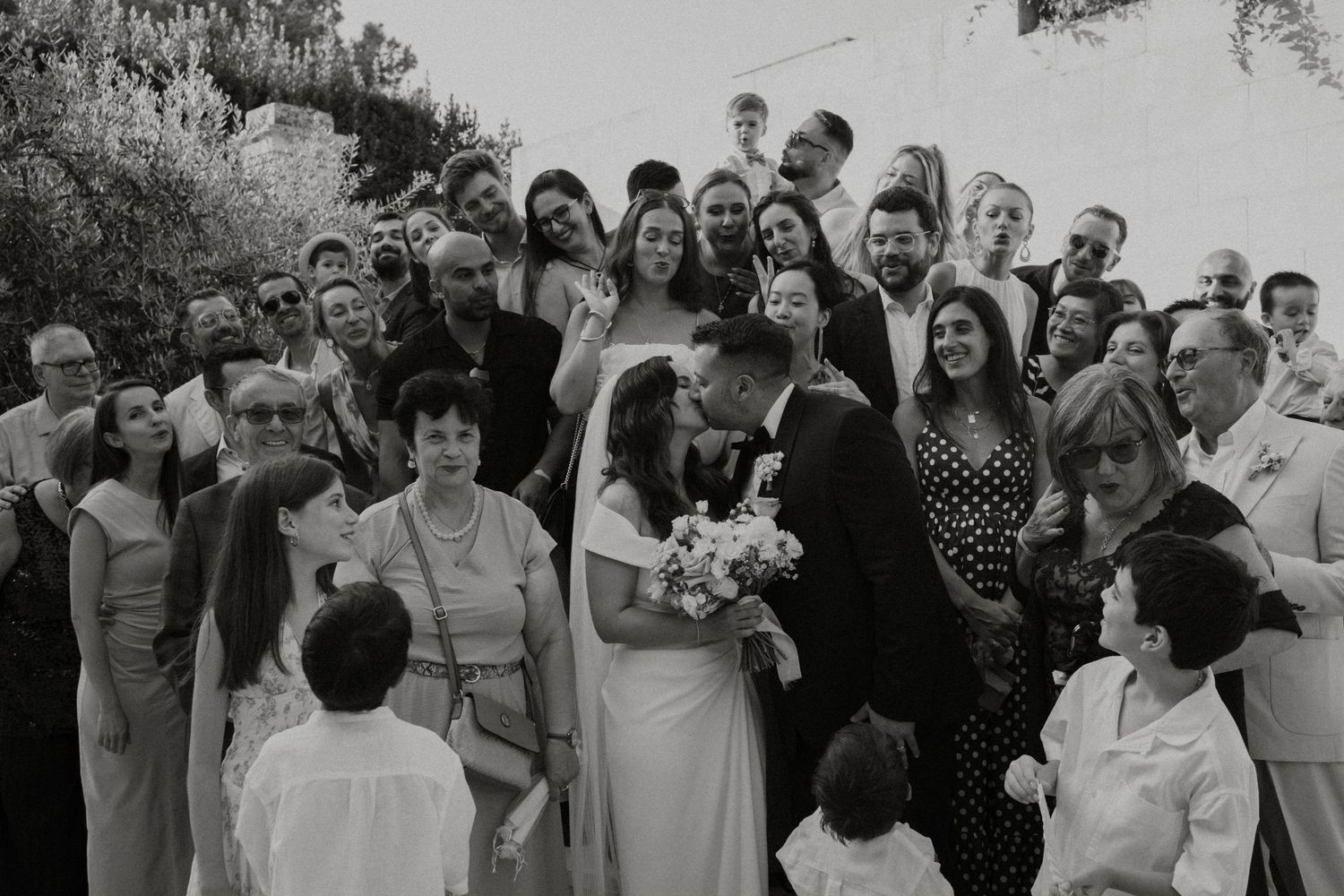 A joyous crowd celebrates outdoors at a wedding reception in black and white.