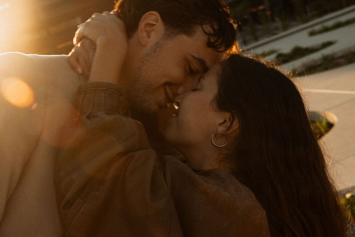 A couple shares a romantic golden hour moment, leaning in for a kiss bathed in warm sunset light.