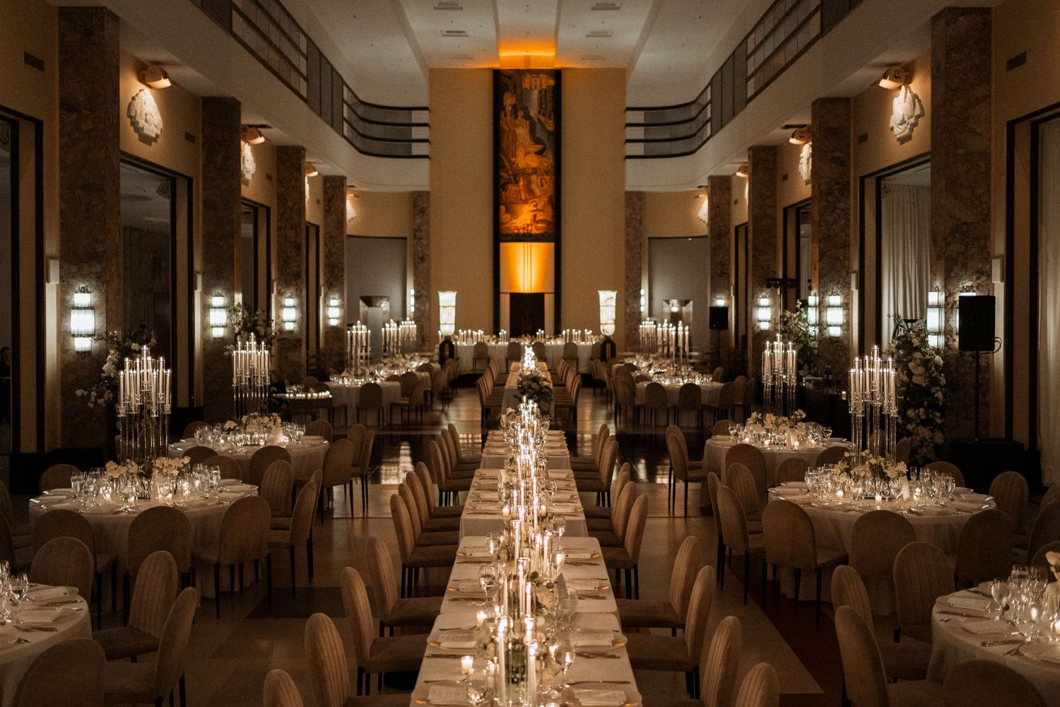An elegant ballroom reception venue with crystal chandeliers and white tablecloths set for a formal dining event.