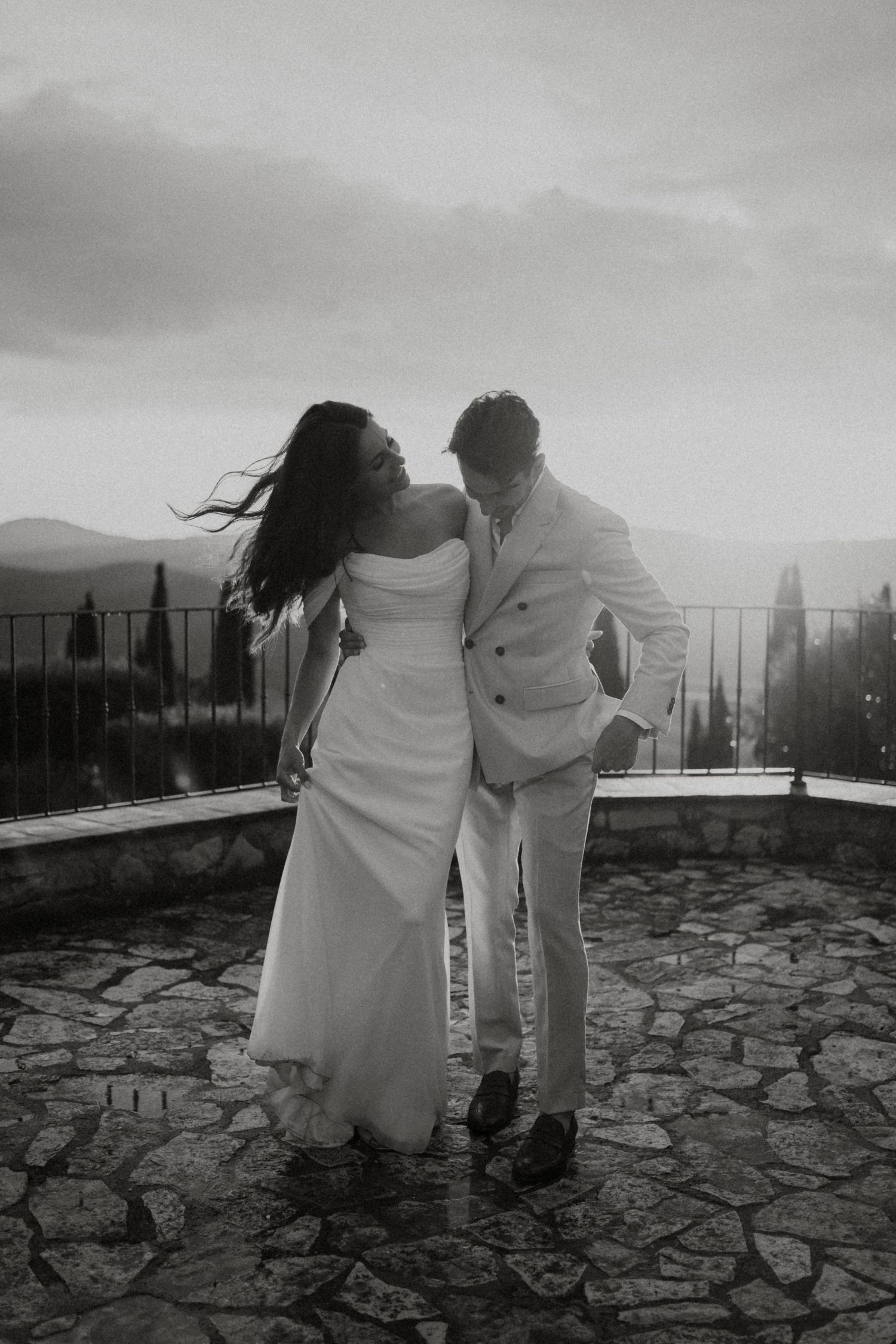 Black and white photos of couple sitting together on stone terrace with scenic view.
