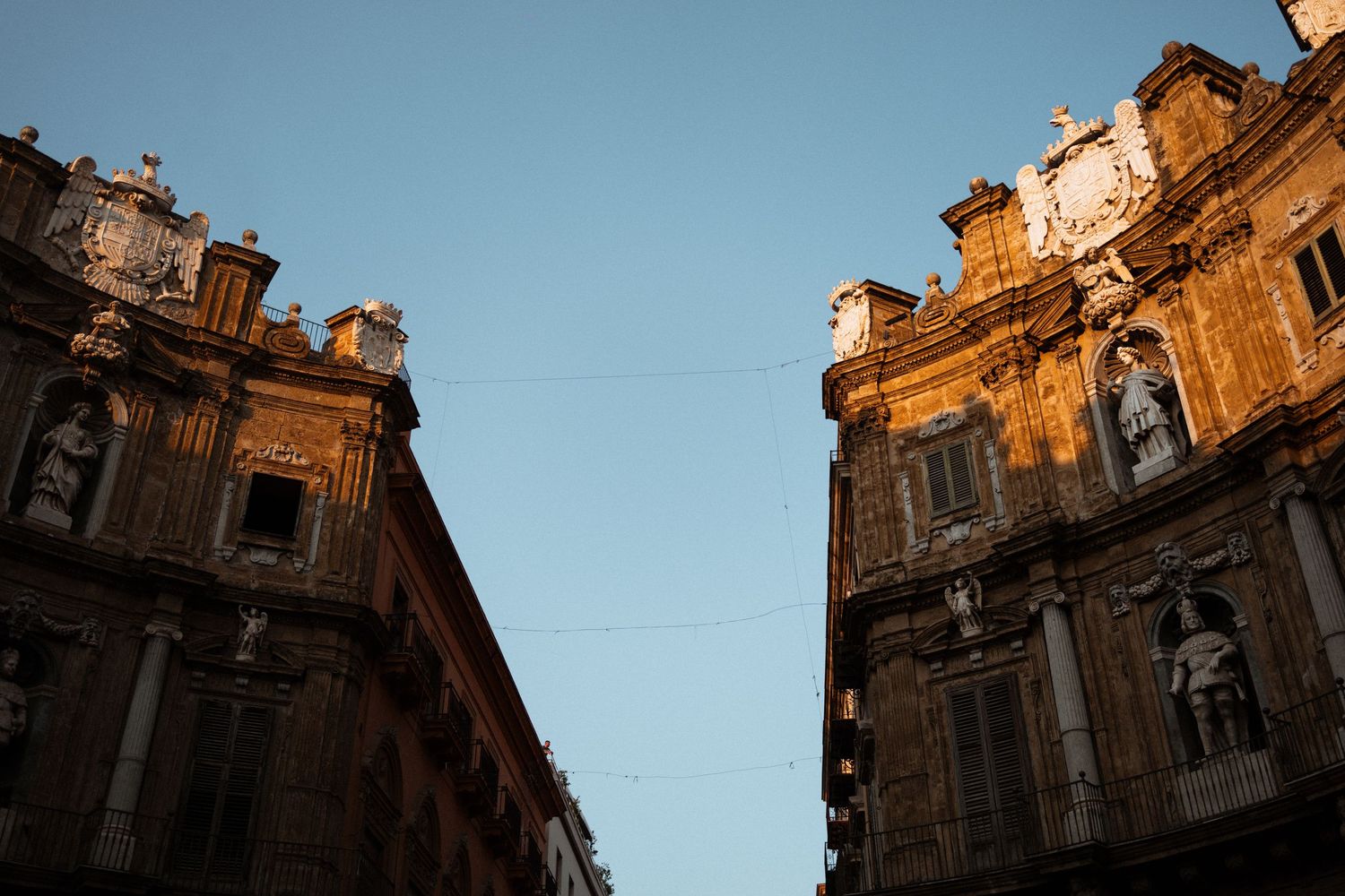 Historic baroque cathedral facade illuminated by golden sunlight against blue sky in Sicily, Italy.