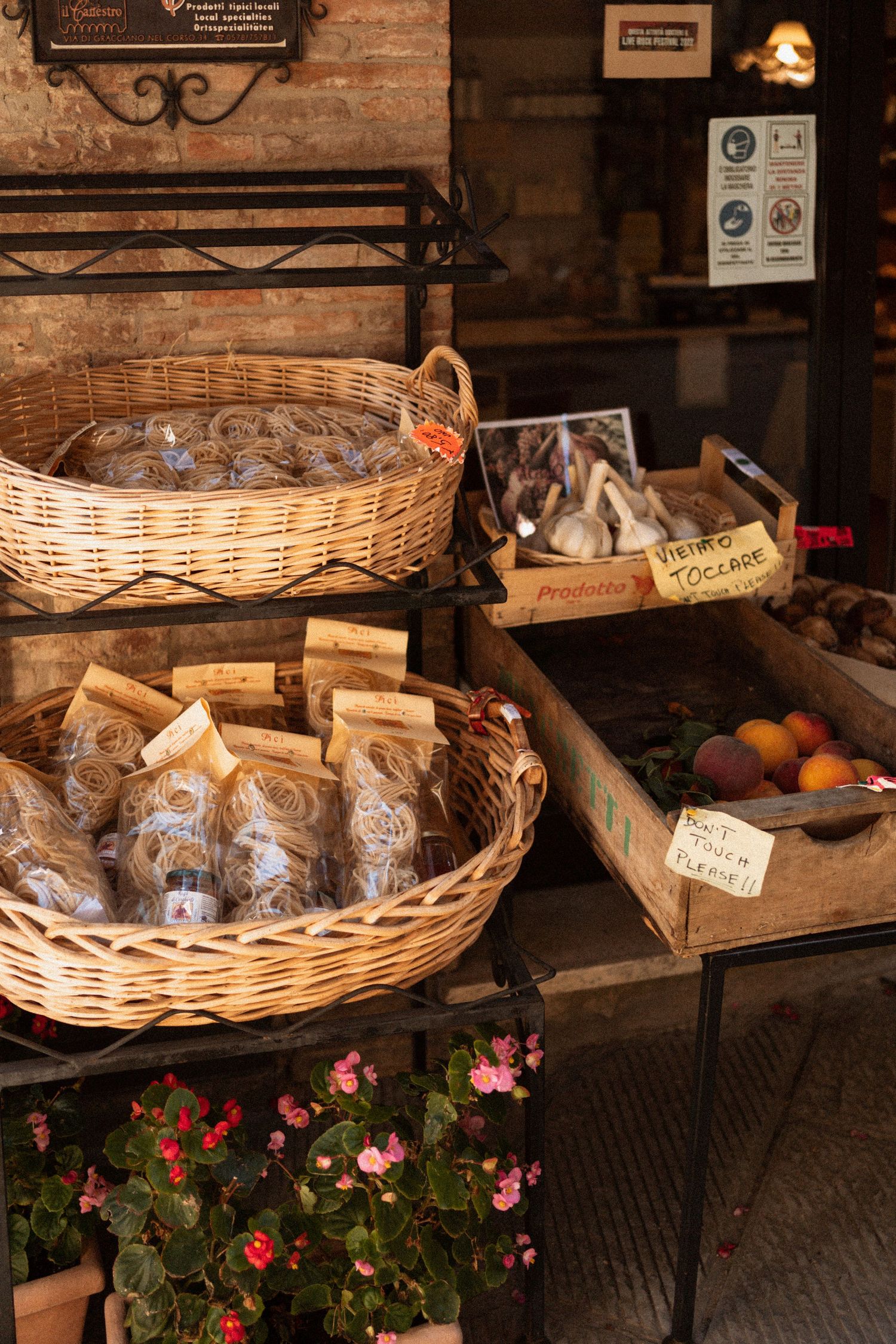 Rustic bakery display with wicker baskets filled with fresh bread and pastries alongside pink flowers in a stone building.