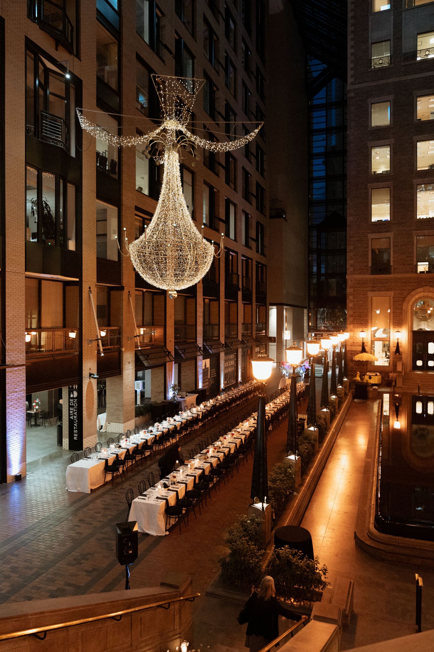 Illuminated outdoor courtyard with hanging angel-shaped holiday lights and white decorative columns between buildings at night.