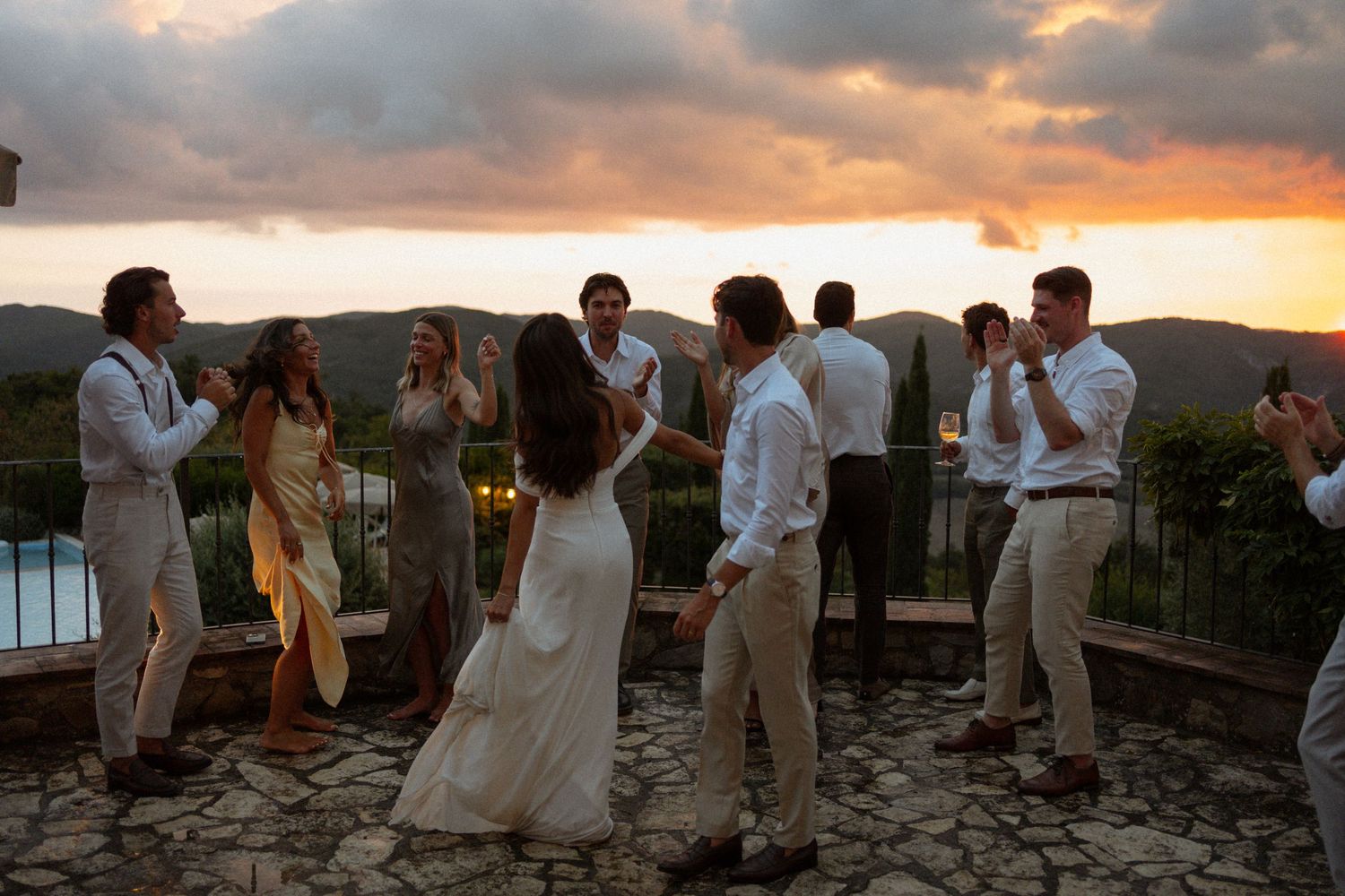 Wedding party gathers on sandy beach during golden sunset with dramatic orange and purple sky.