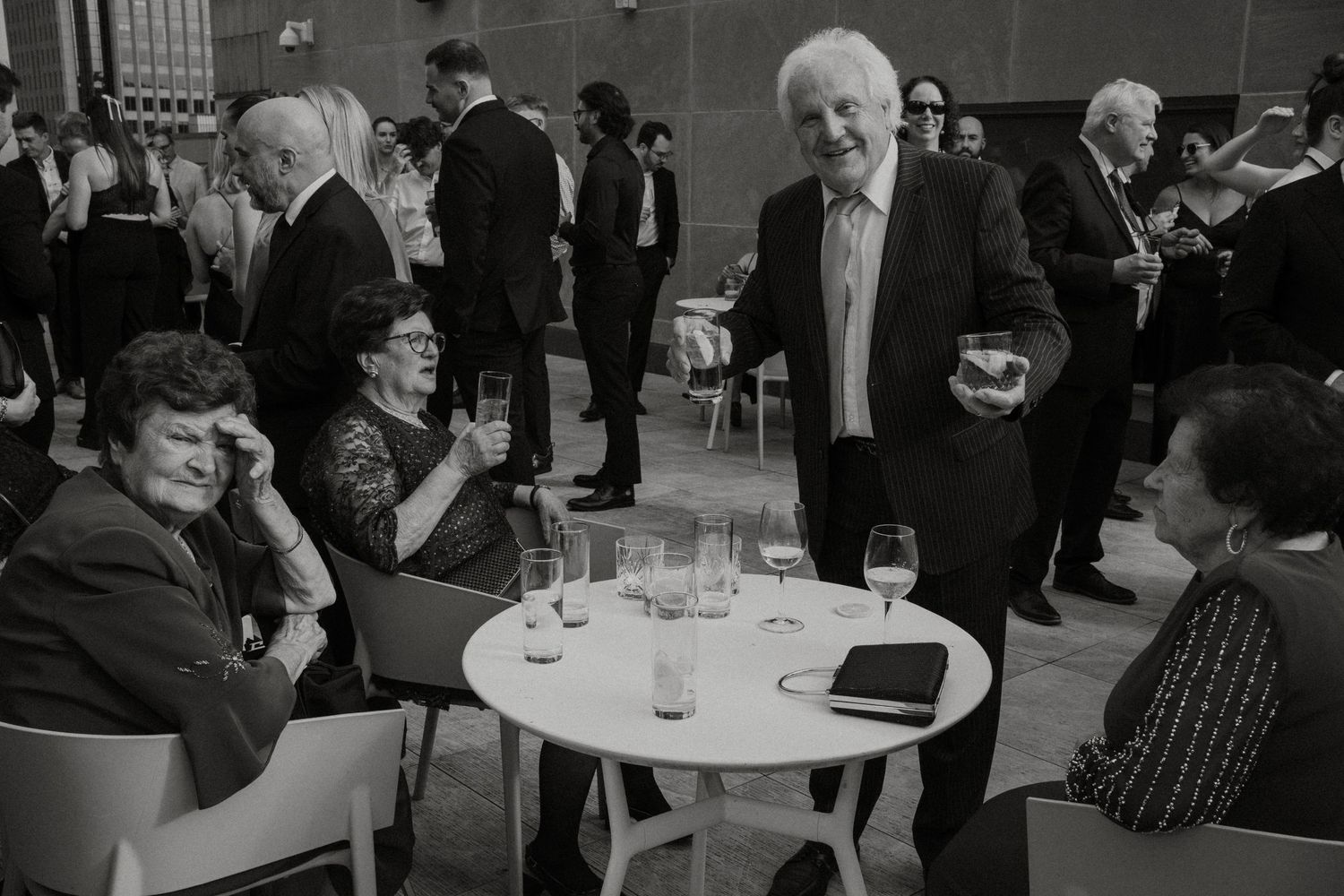 Black and white photo showing people mingling at a formal social gathering in an indoor venue.
