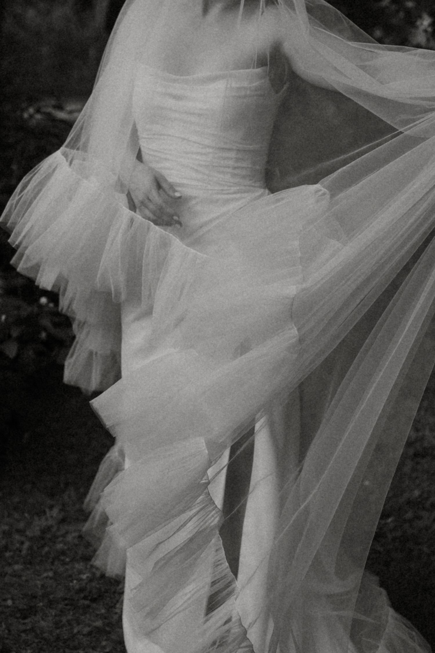 A flowing white wedding dress veil blows gracefully in the wind creating an ethereal effect in black and white photography.