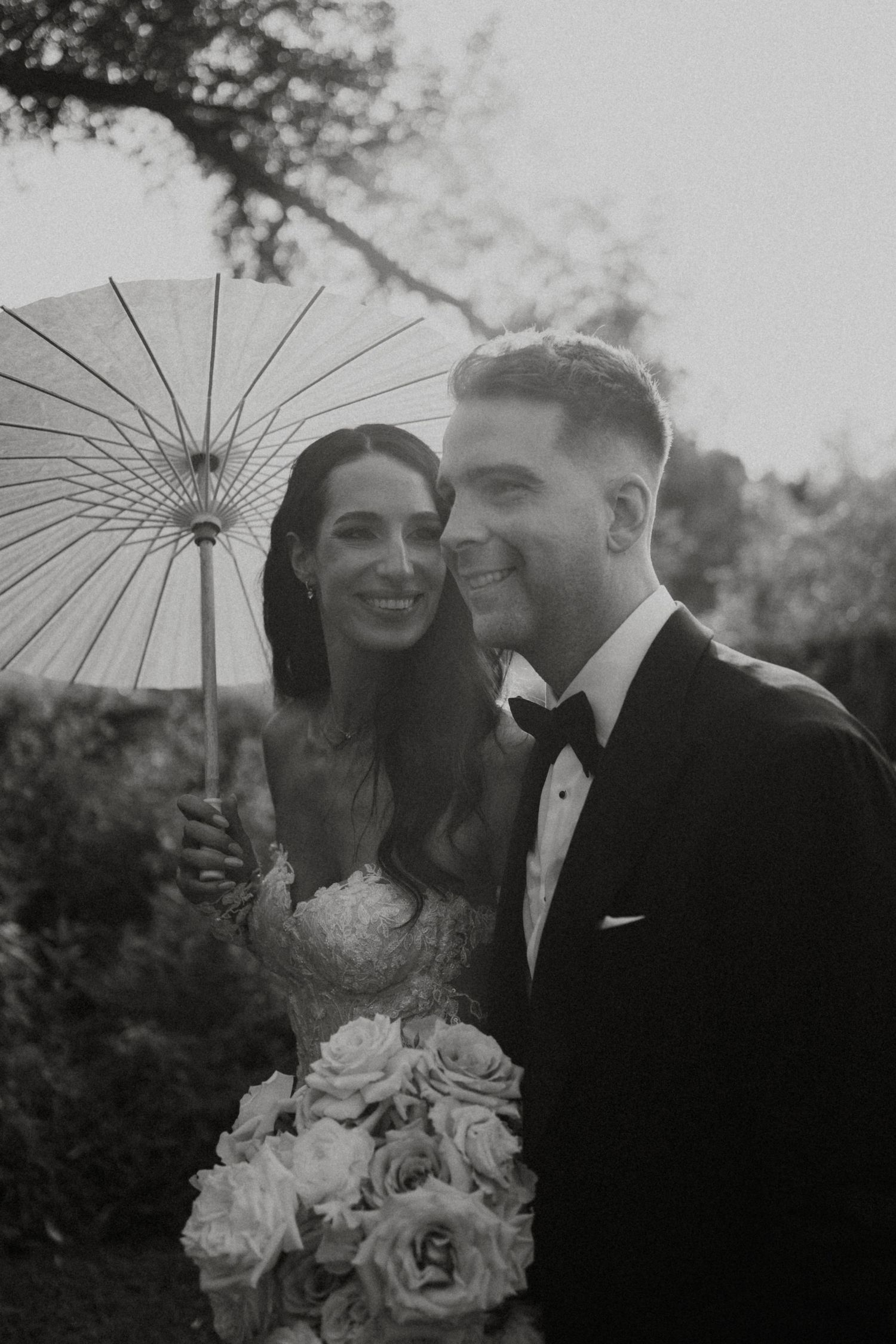 Romantic black and white portrait with decorative parasol and floral bouquet.