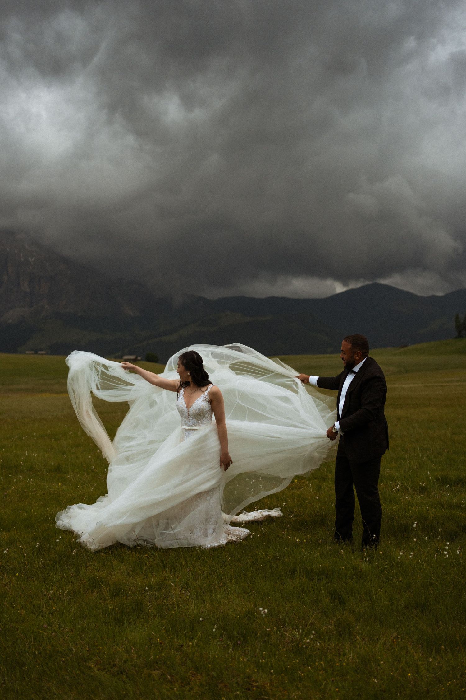 Dramatic wedding photo with flowing white dress against stormy mountain landscape.