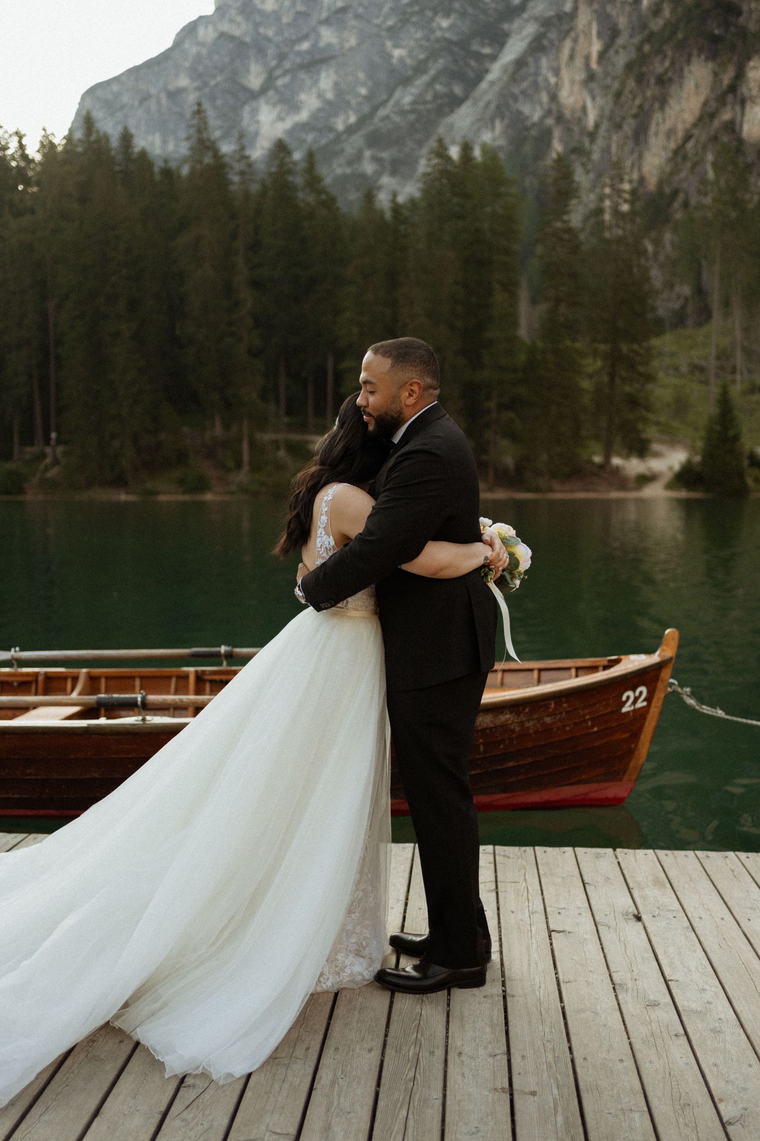 A romantic moment captured on a wooden dock by a lake surrounded by mountains.