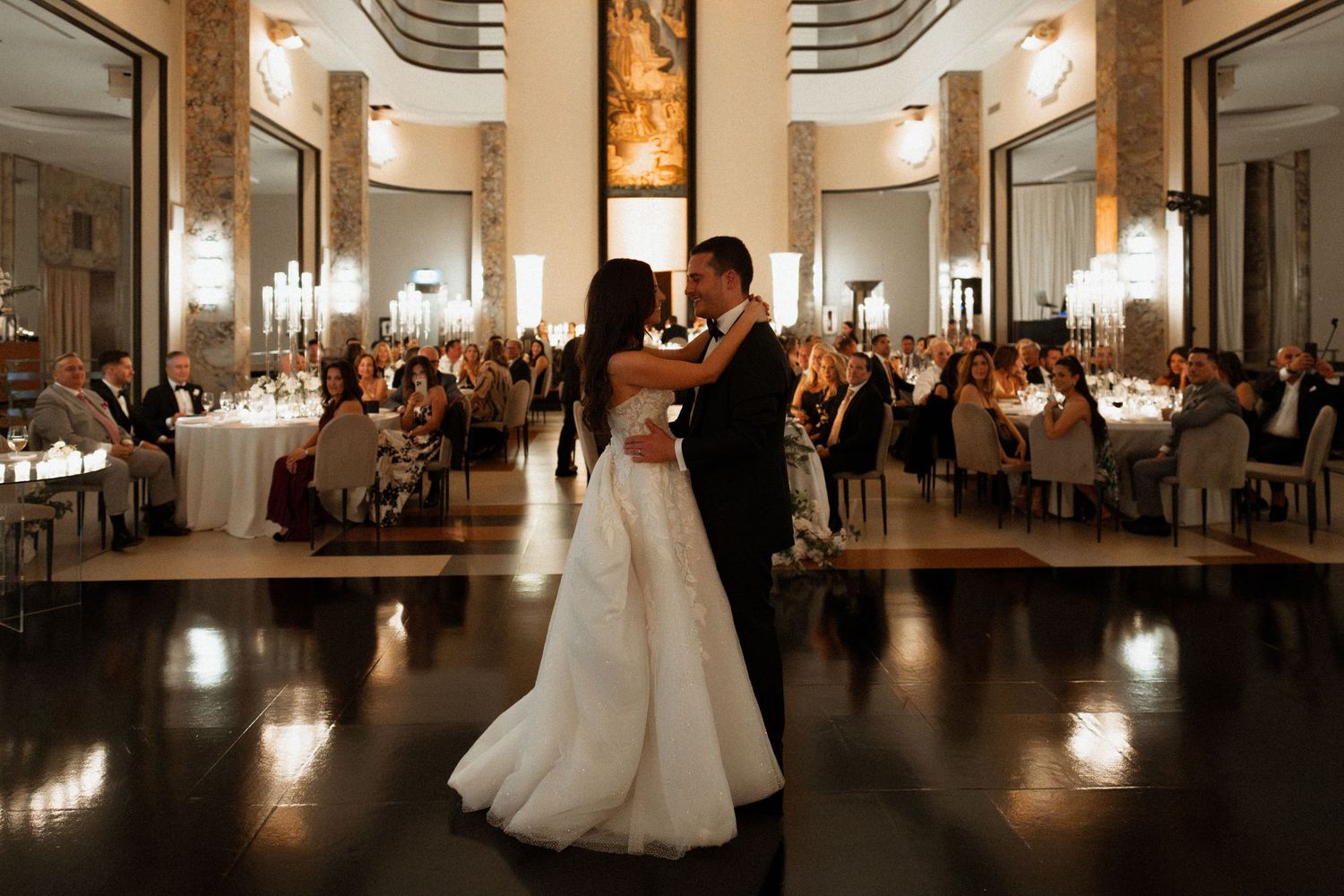 Elegant wedding reception venue with couples dancing in a grand ballroom illuminated by warm lighting.