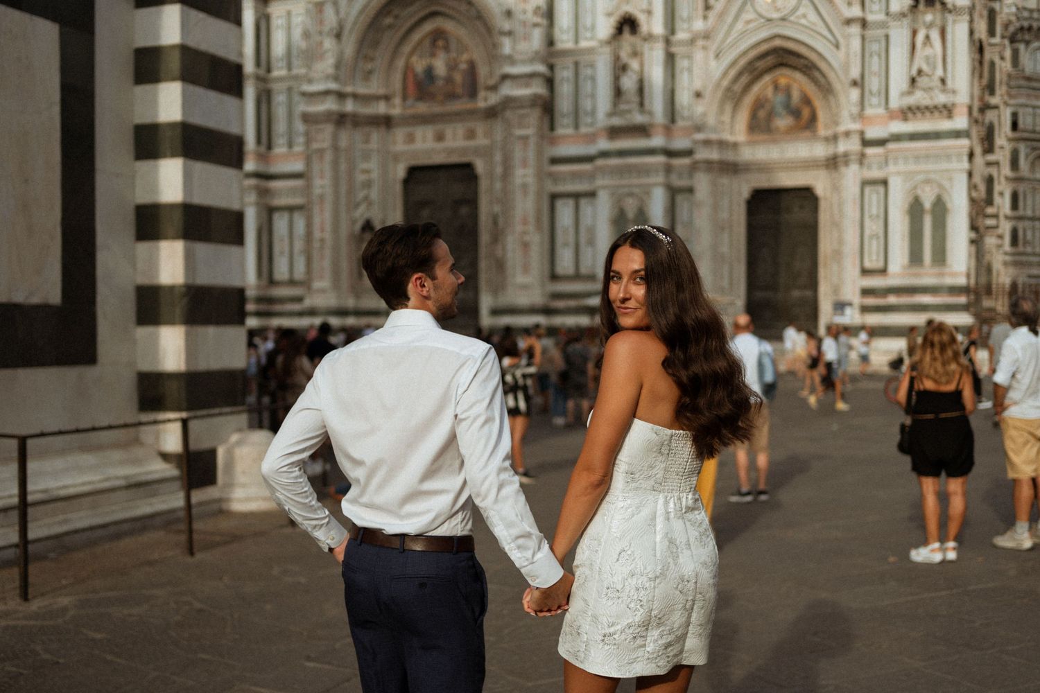 Couple walks hand in hand through the historic streets of Florence, Italy with the Duomo cathedral in the background.