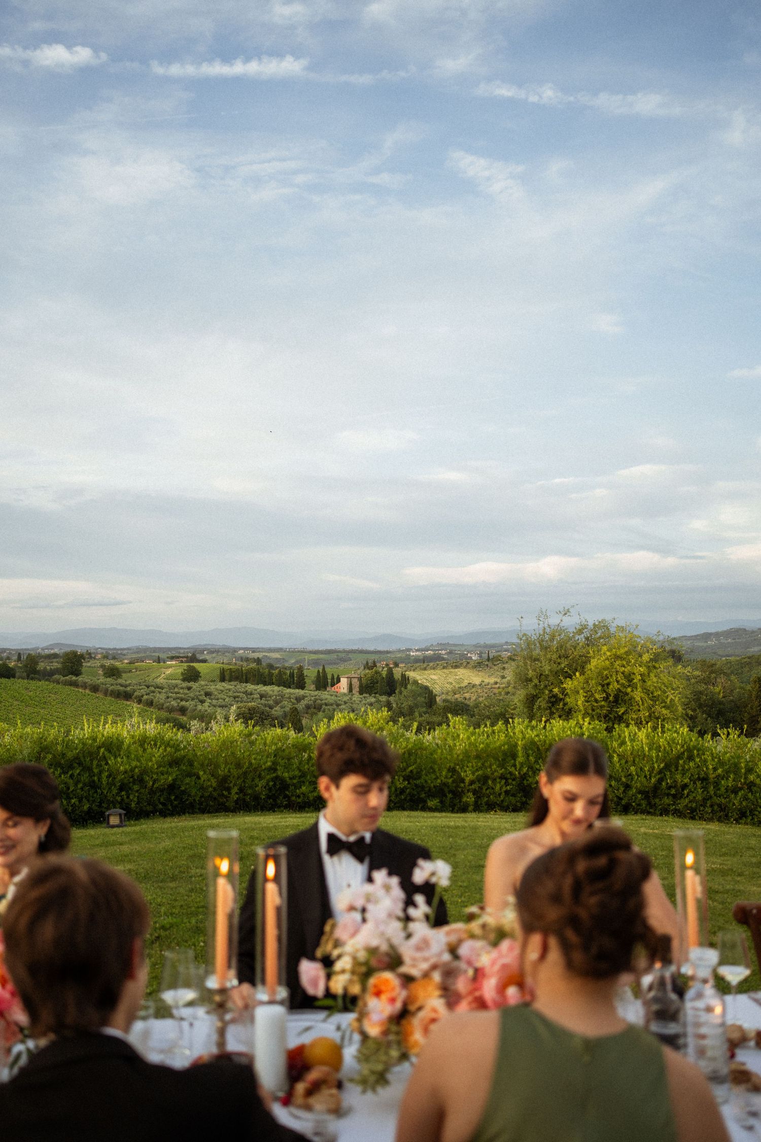 Elegant outdoor wedding reception in Tuscany with candlelit table, floral centerpiece, and rolling vineyard hills at dusk.