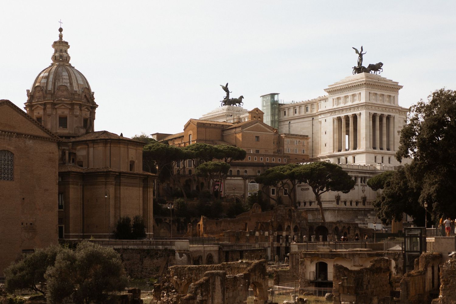Ancient ruins and monuments of the Roman Forum in Rome, Italy with the Victor Emmanuel II Monument visible in background.