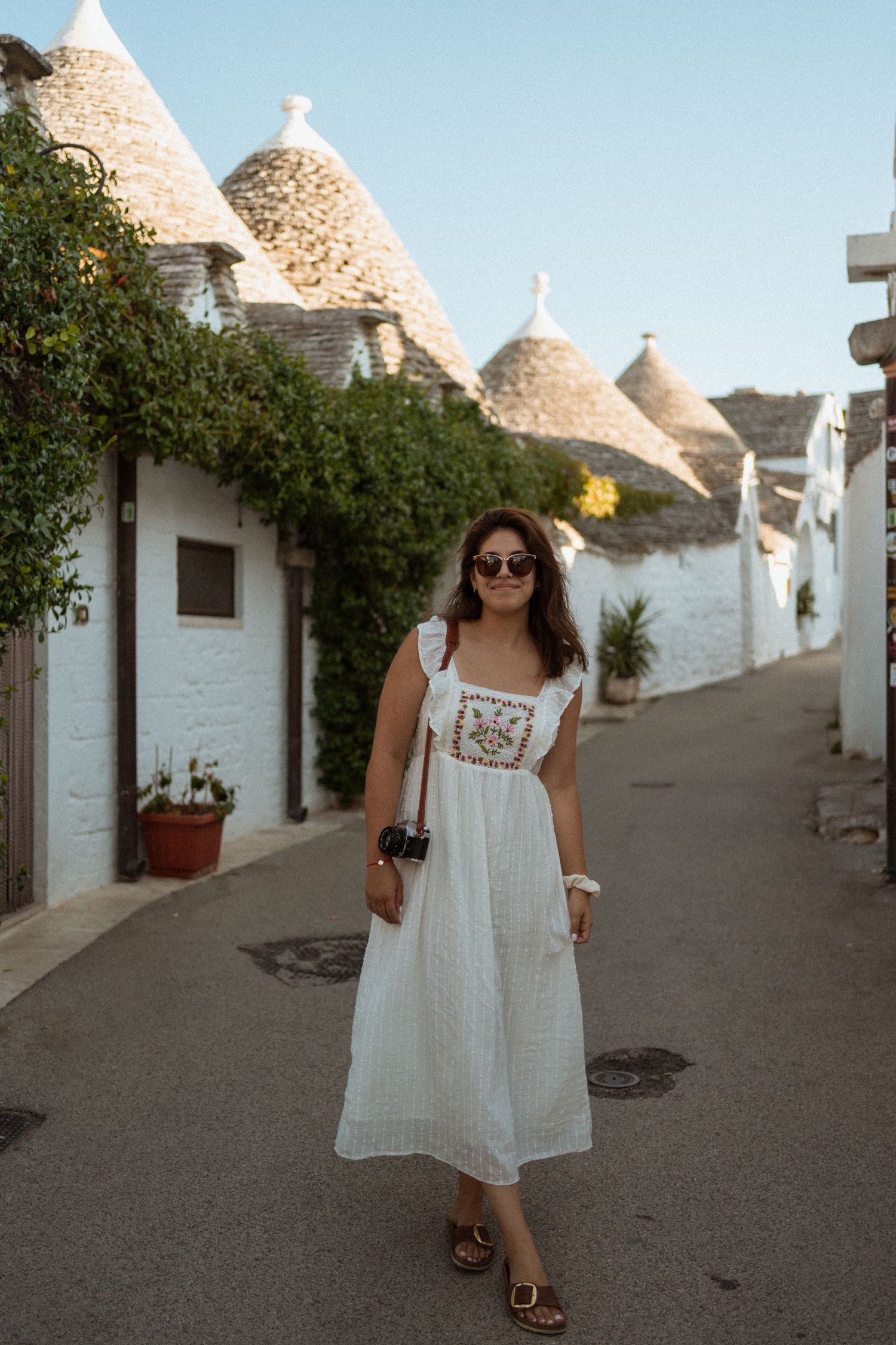 White traditional trulli houses with conical roofs line a narrow street in Alberobello, Italy during golden hour.