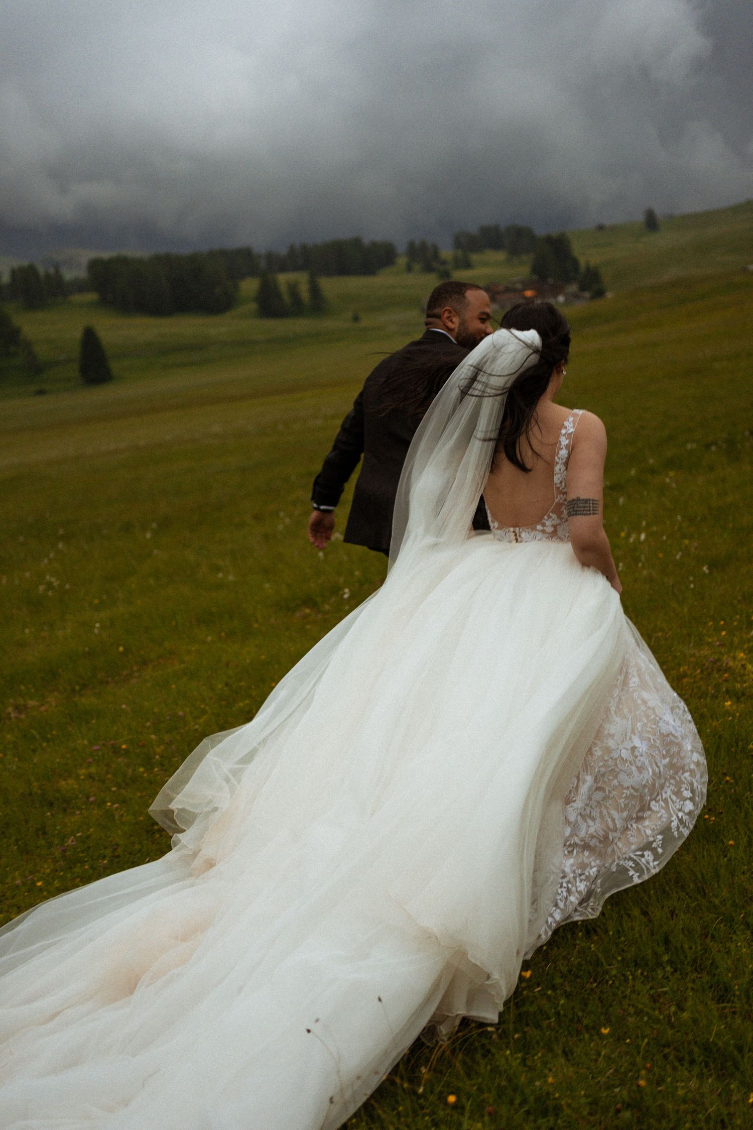 A flowing white wedding gown with lace details moves gracefully across a mountain meadow.
