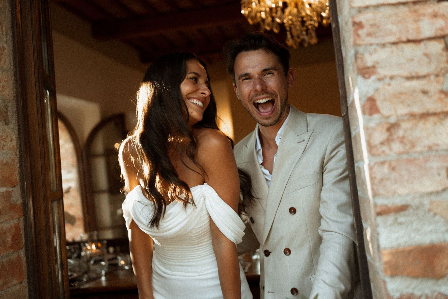 A couple shares a joyful moment together in front of a rustic brick wall background.