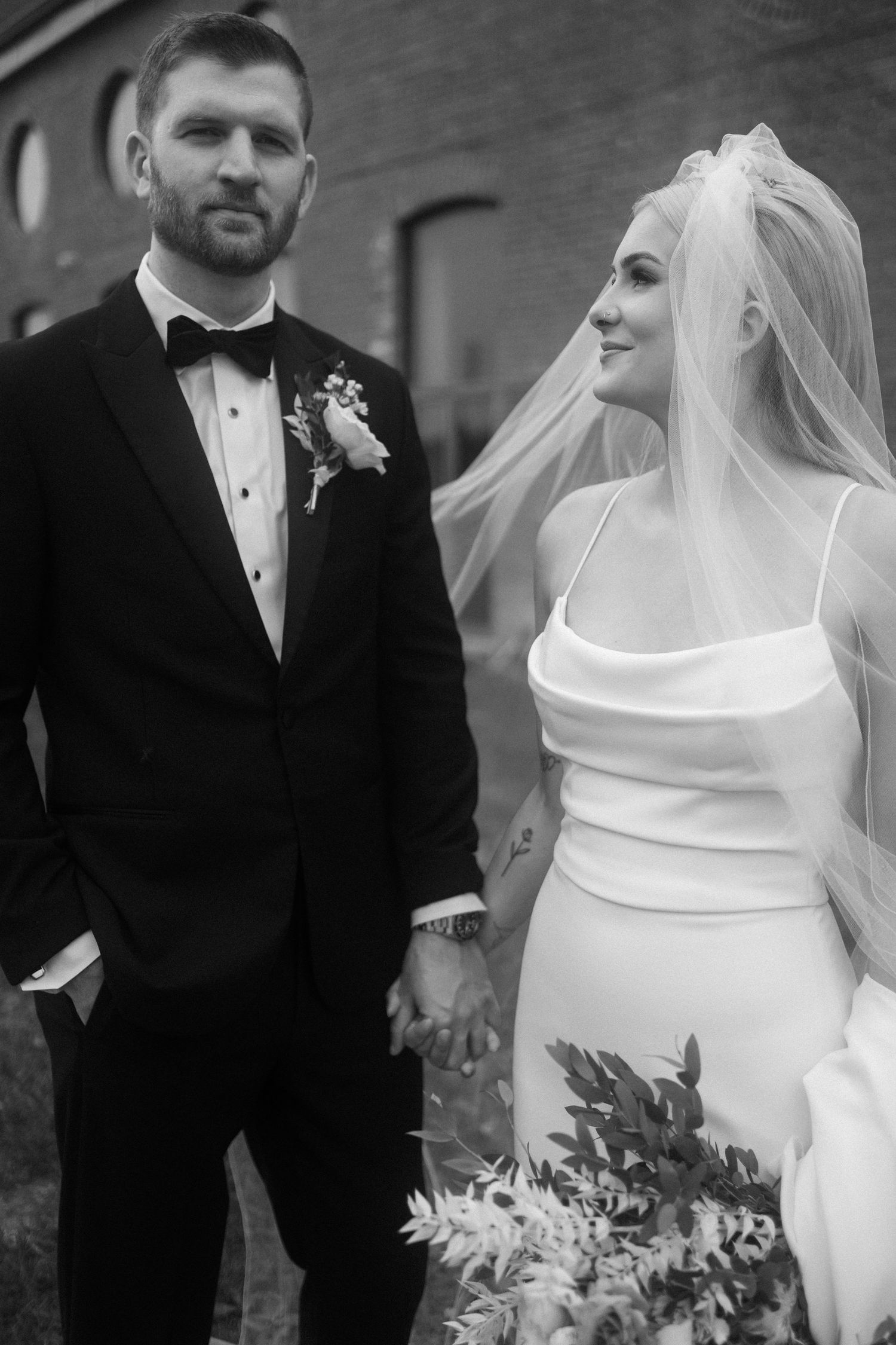 Elegant black and white portrait of newlyweds with minimalist wedding attire and floral bouquet.