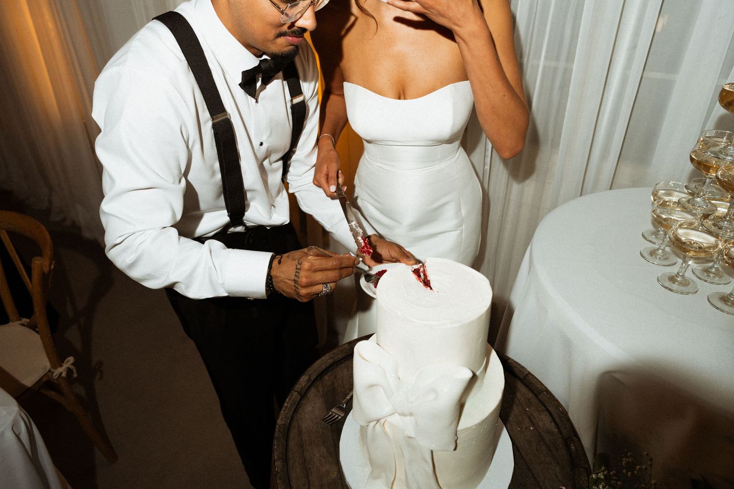 Bride and groom cutting white three-tier wedding cake together at elegant reception venue.