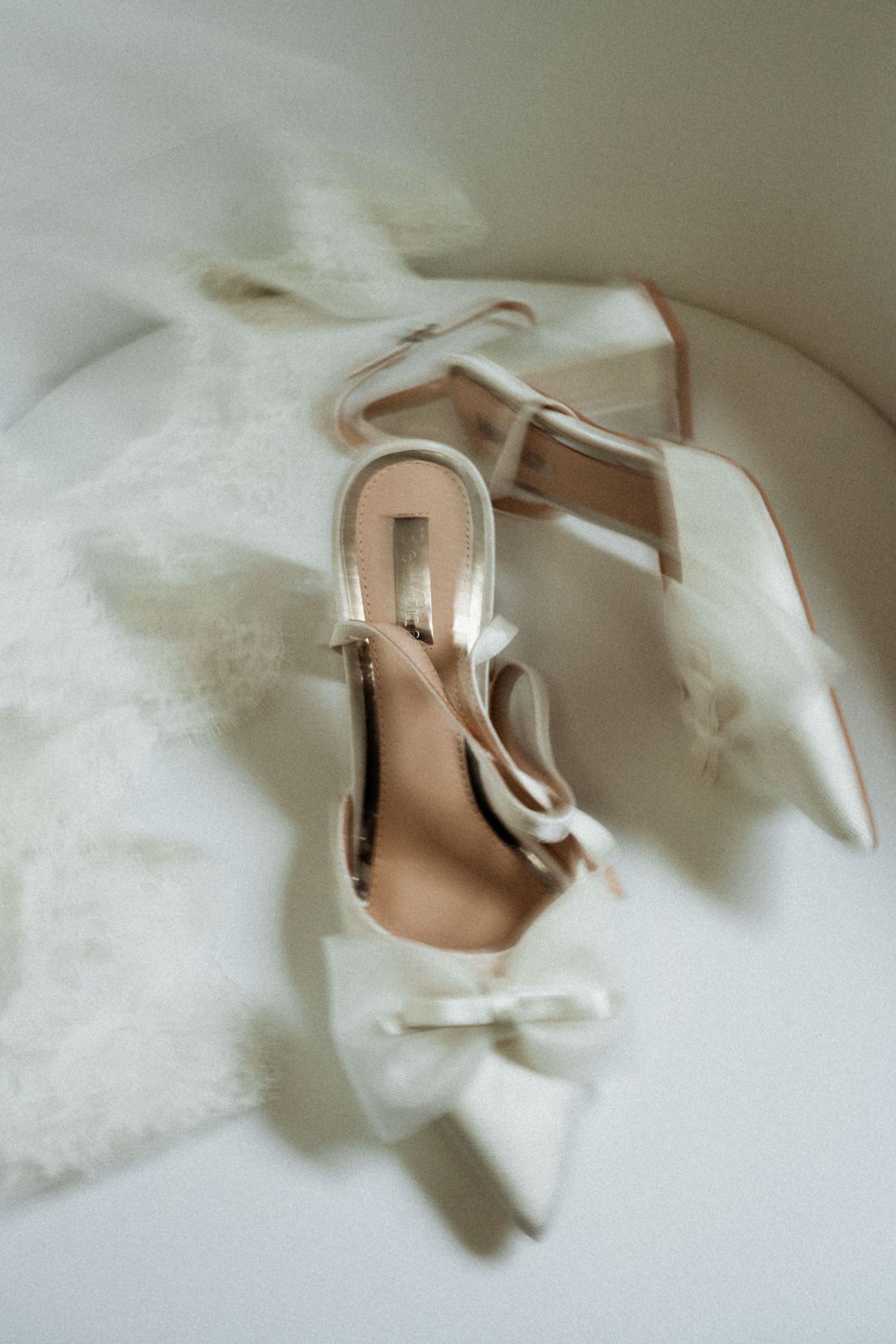 Elegant nude-colored bridal shoes nestled in soft white fabric creating a romantic wedding detail shot.