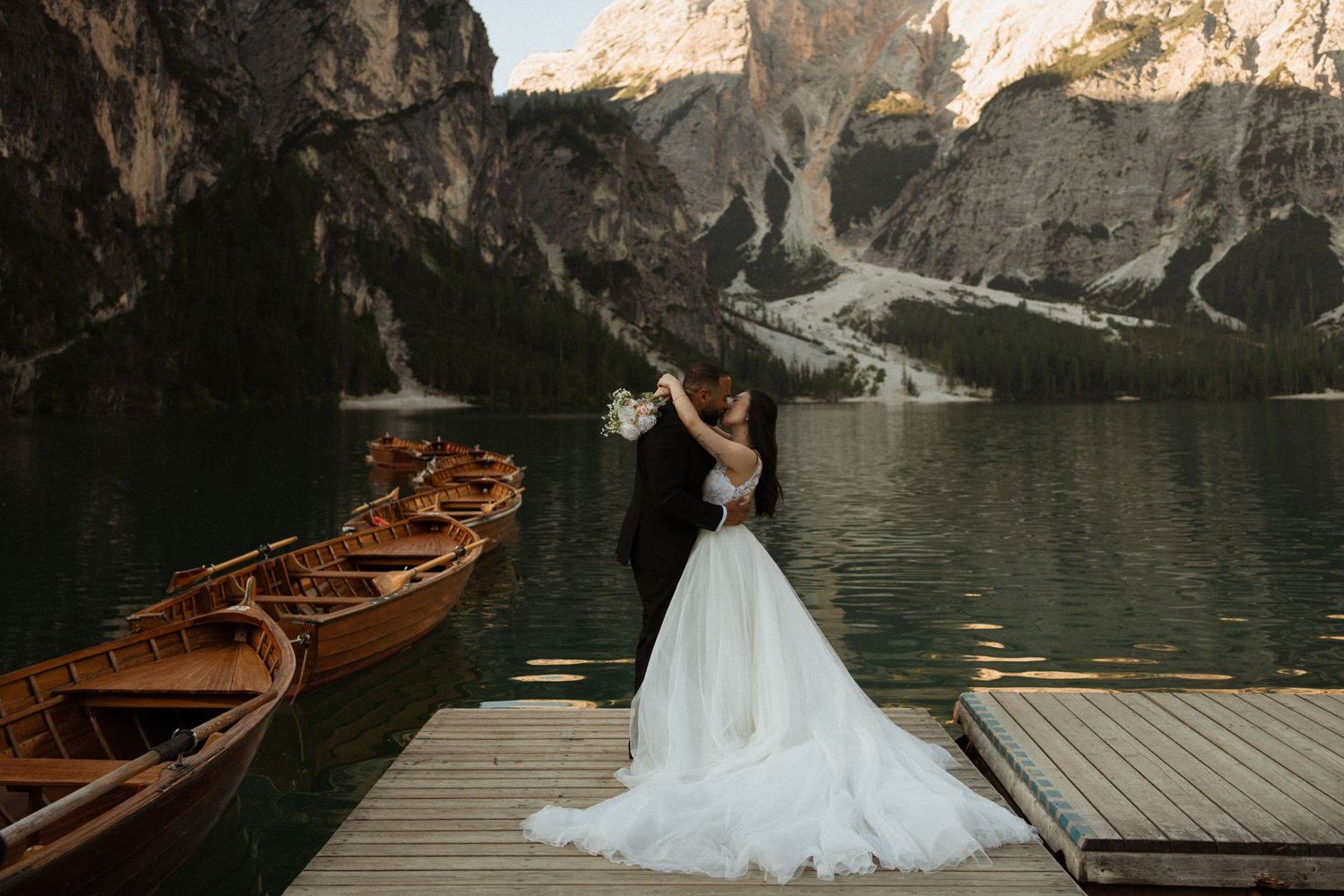 Wooden boats docked at a scenic mountain lake with dramatic rocky cliffs and calm waters reflecting the landscape.
