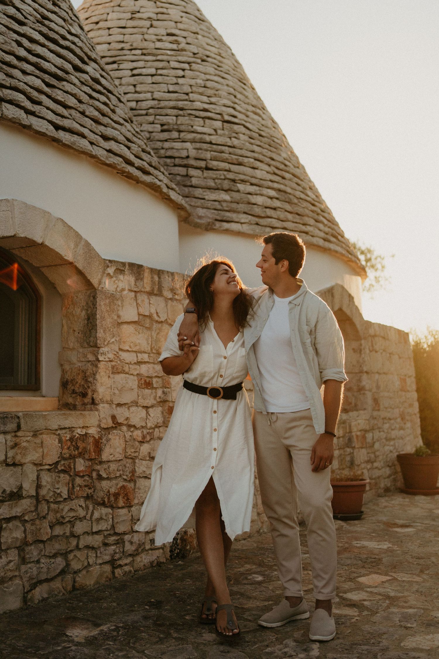 Couple embracing at golden hour beside a traditional trullo stone building in Alberobello, Italy.