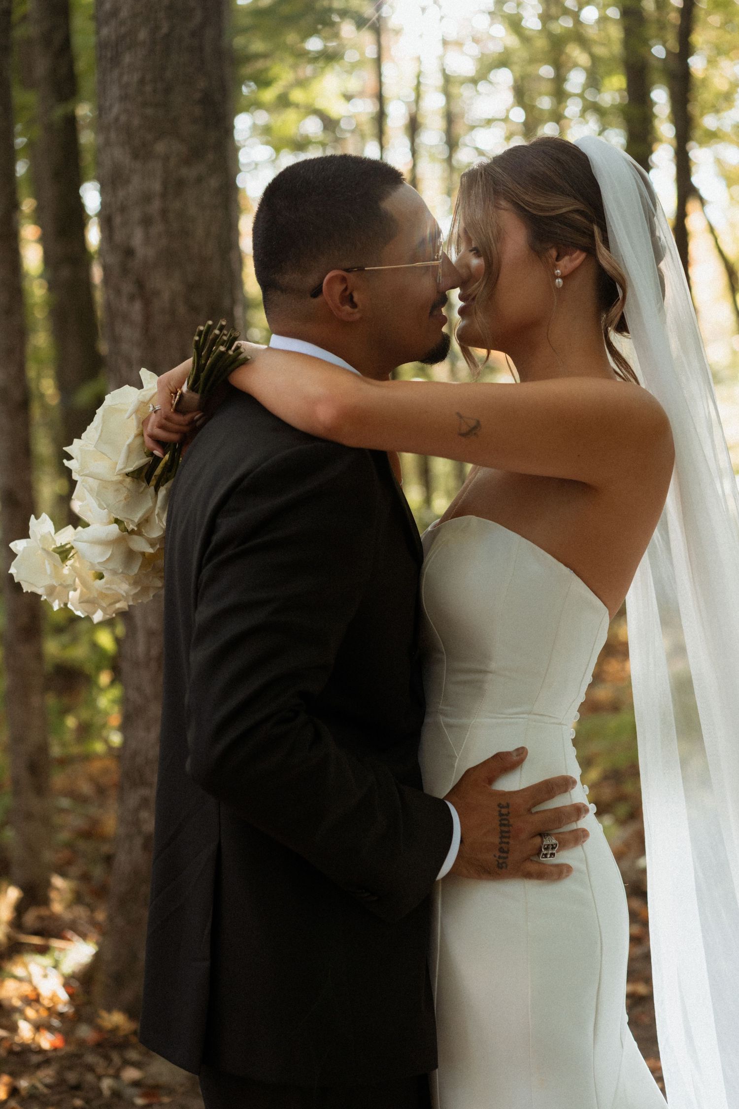 Romantic wedding couple embracing in a sunlit forest setting.