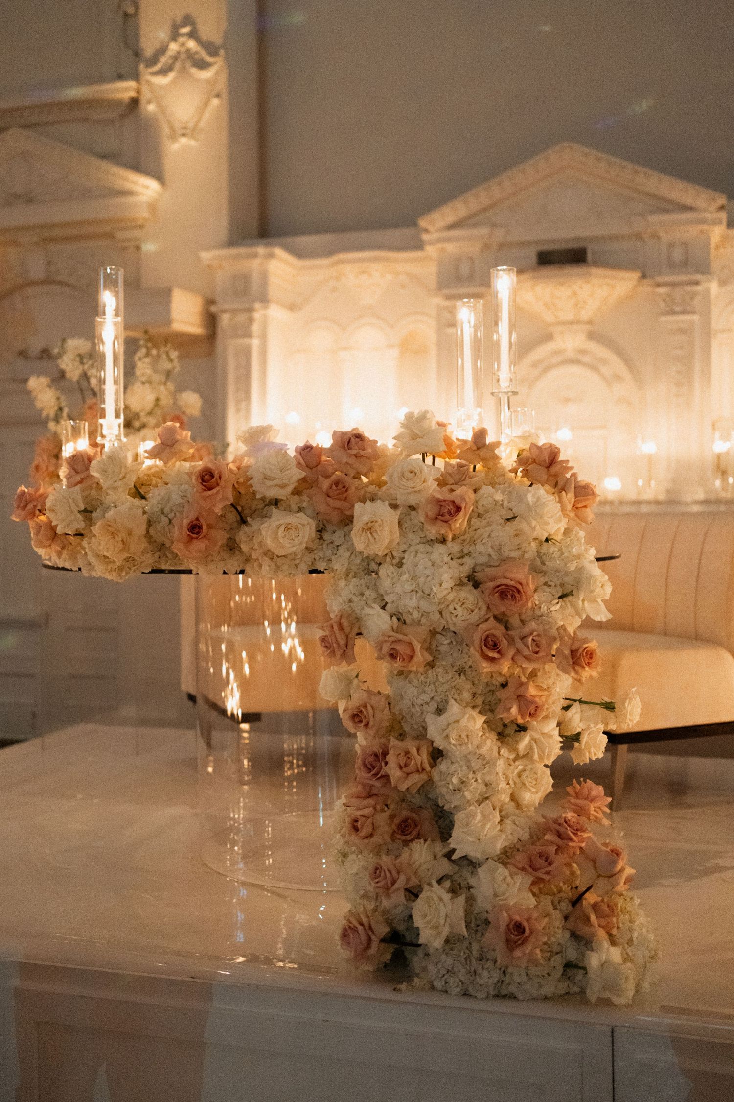 Elegant floral centerpieces with white and peach roses line a long banquet table in a luxurious ballroom setting.