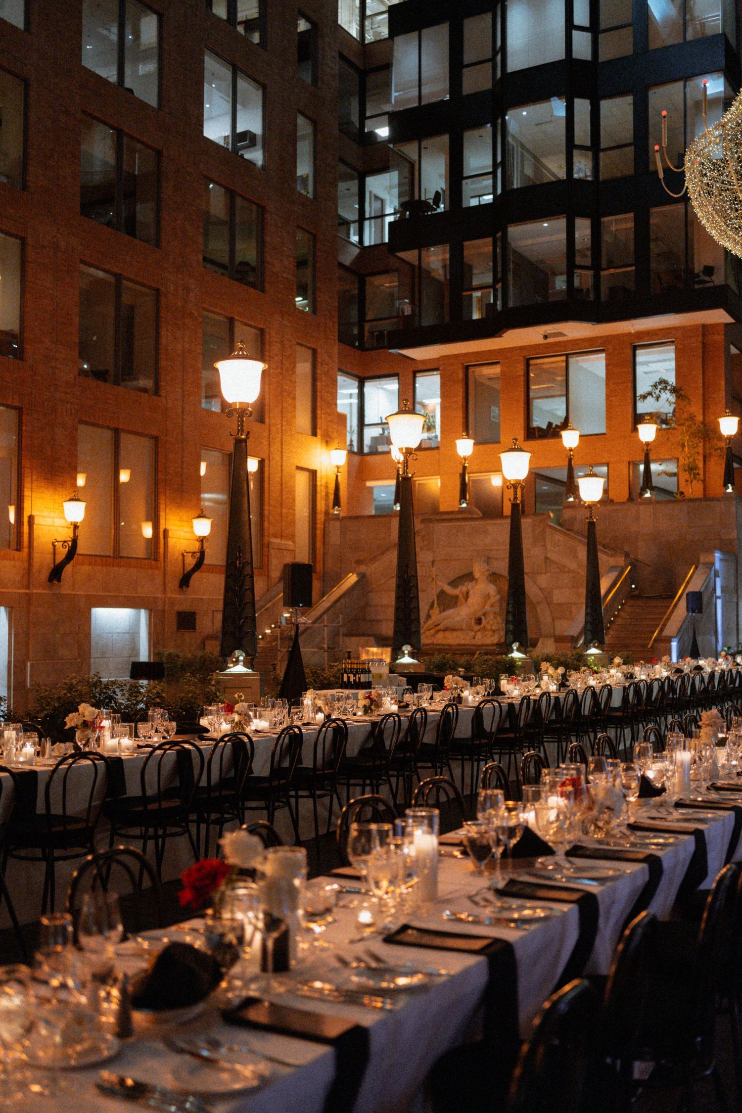 Elegant candlelit dining tables set for a formal event in an industrial brick venue with warm ambient lighting.