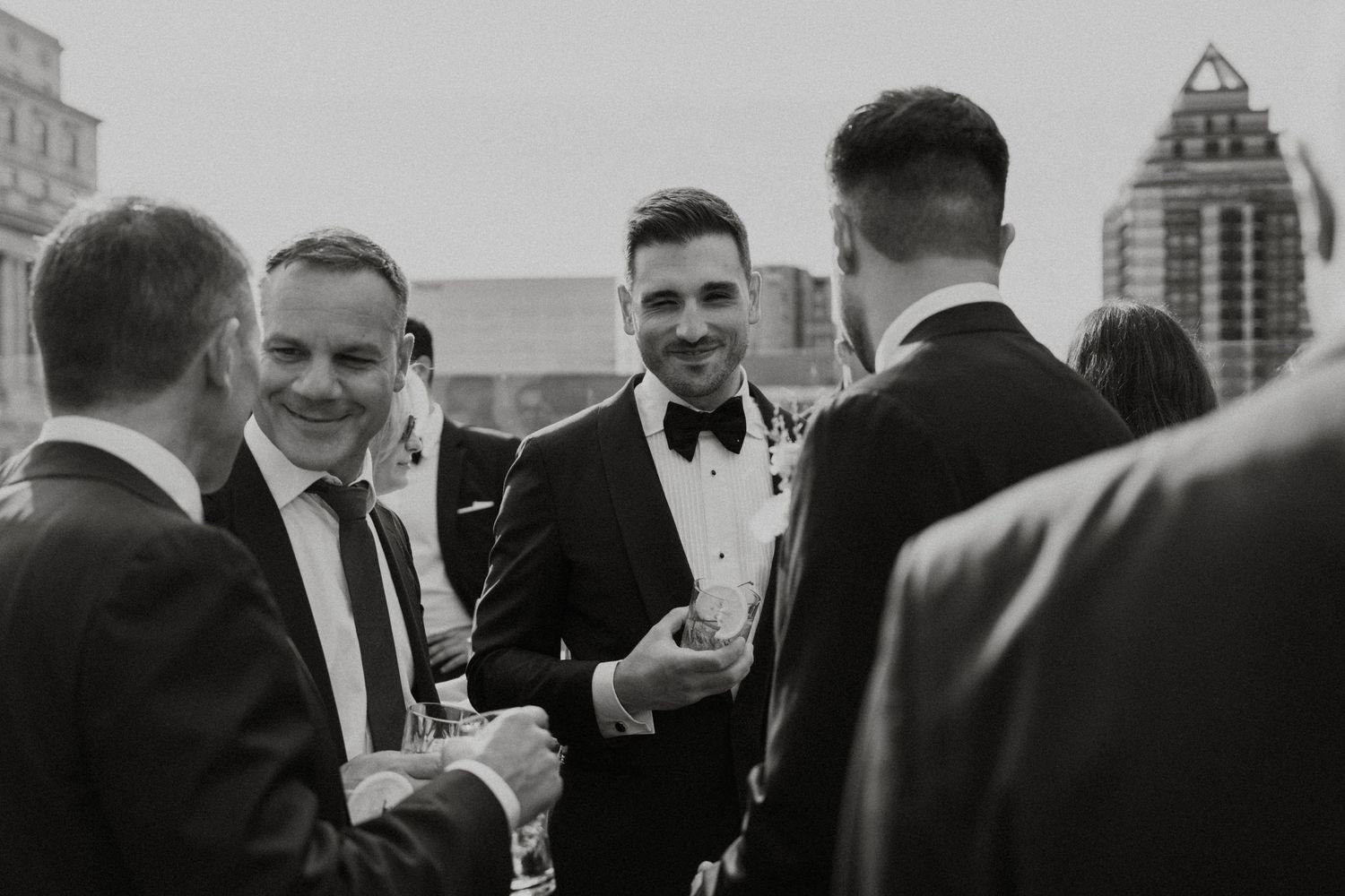 A black and white photograph of people in formal attire having a conversation at an outdoor event.