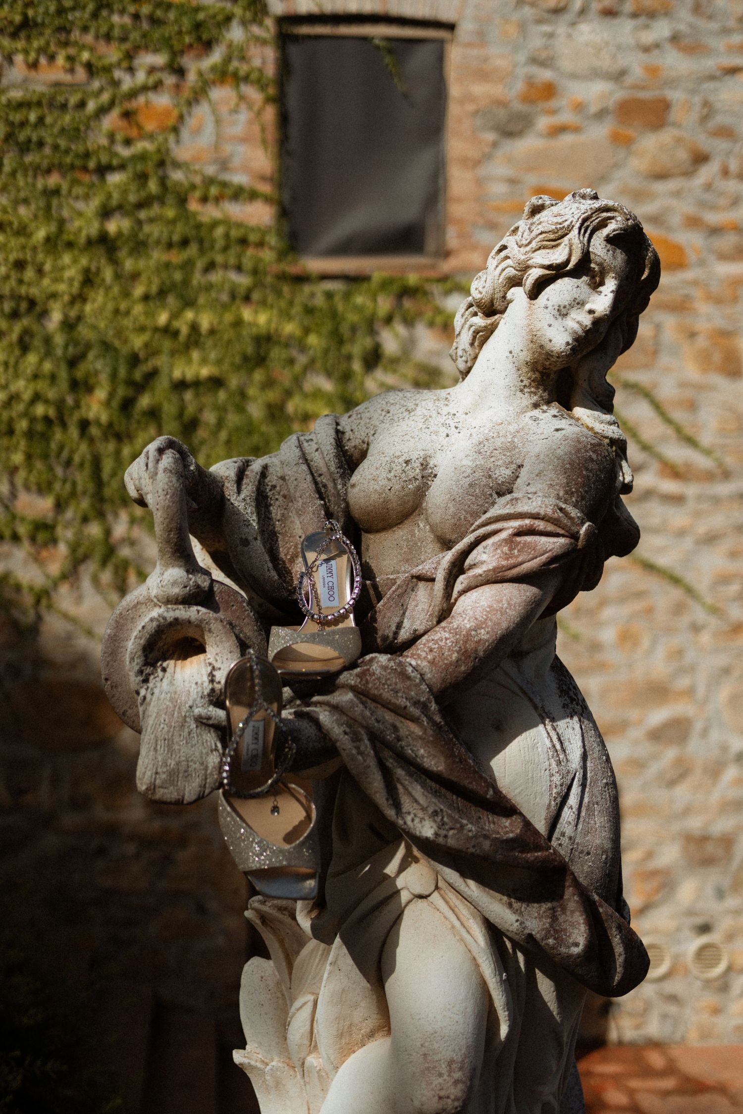Weathered stone statue of an angel with dramatic pose against an old brick wall covered in ivy.