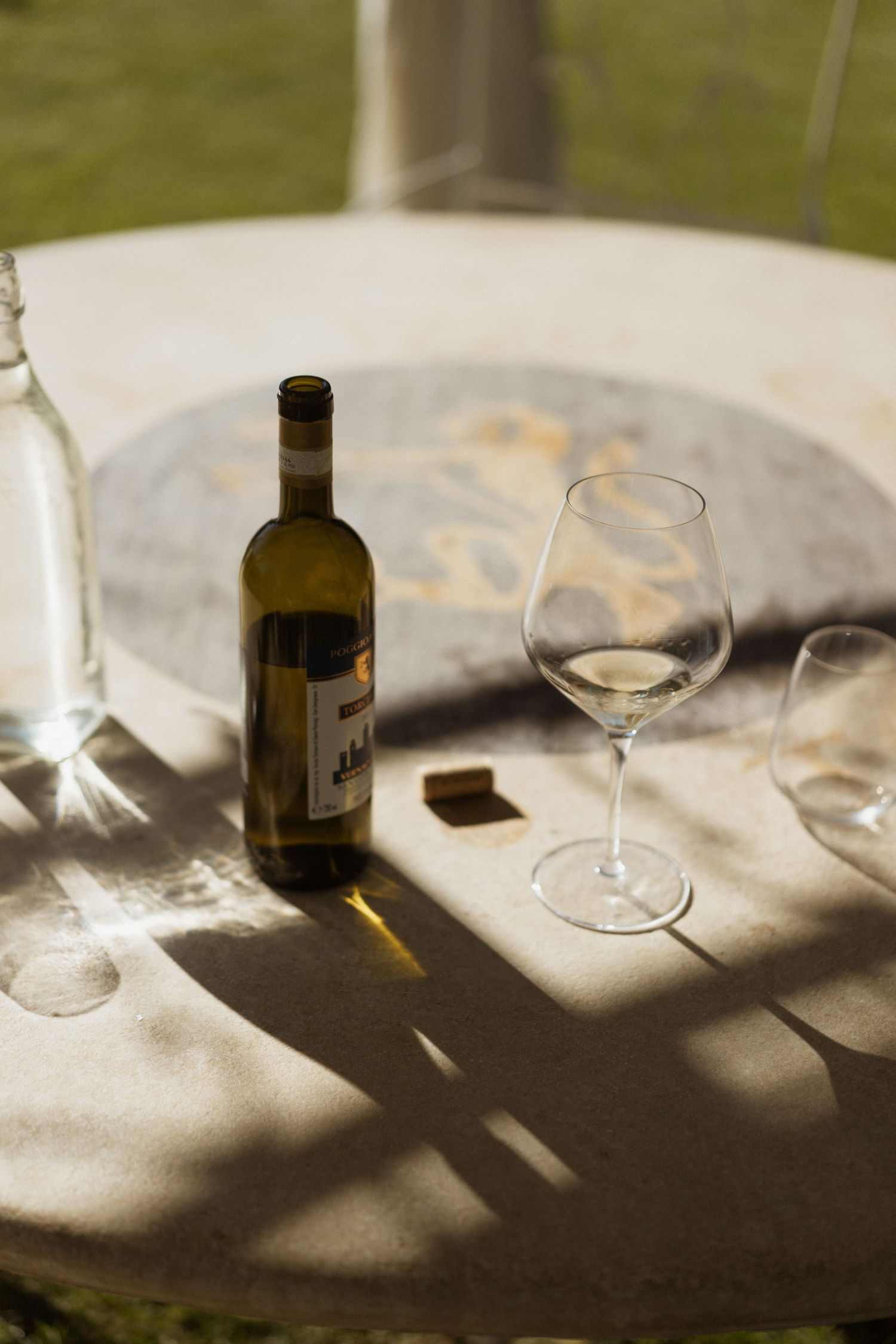 Shadows cast by wine glasses and bottles create an artistic pattern on a light-colored tablecloth in natural sunlight.