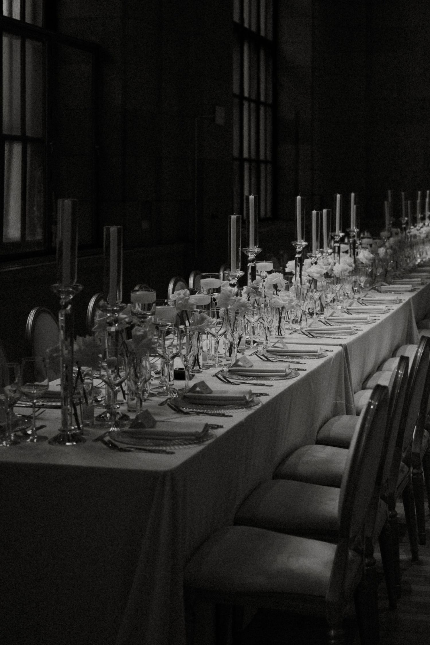 Long formal dining table set with white linens and glassware in a dimly lit elegant restaurant space.