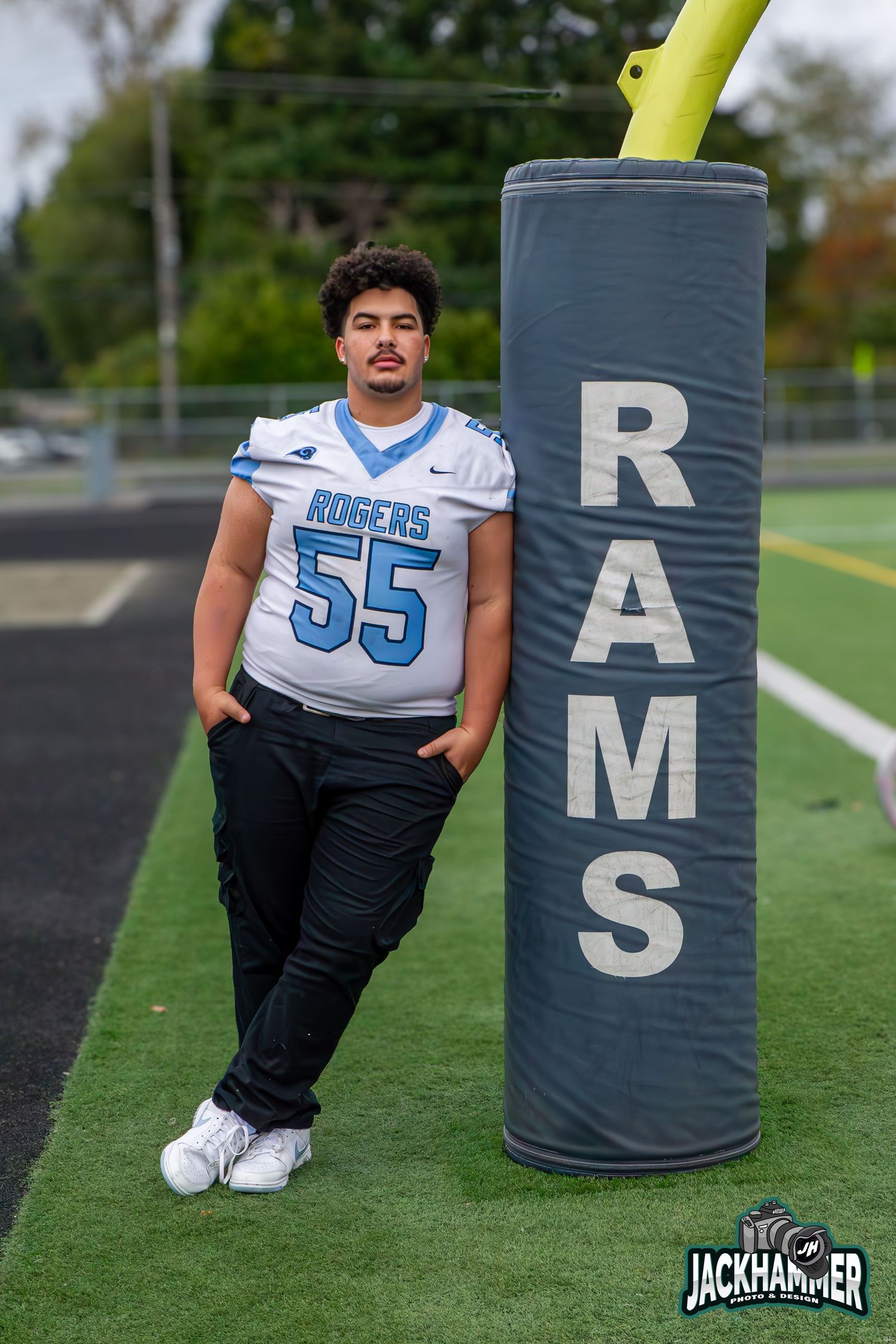 High school football player number 55 in Rogers Rams jersey leaning on a training dummy on field.