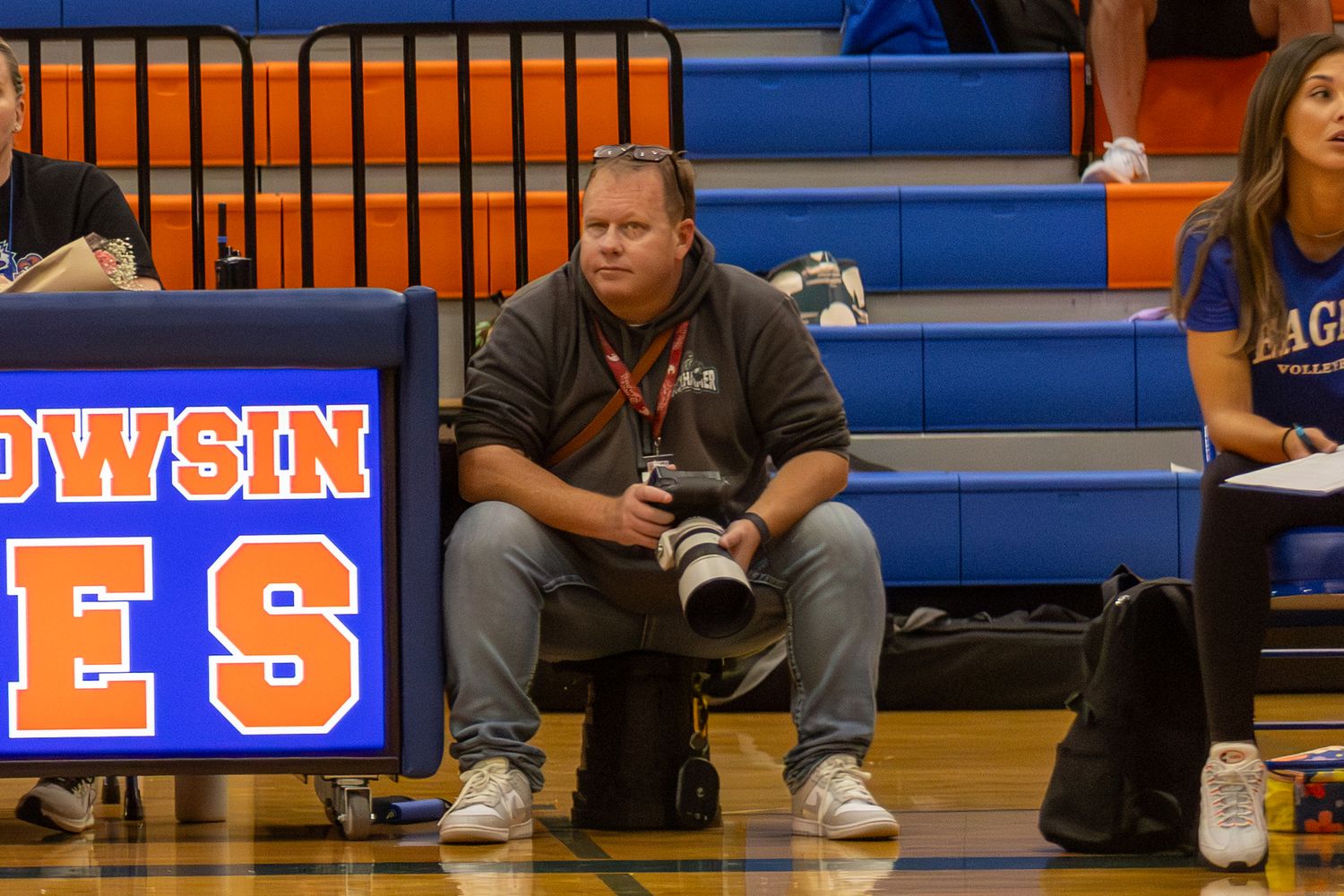 Professional photographer with a telephoto lens sitting courtside at an indoor high school basketball game.