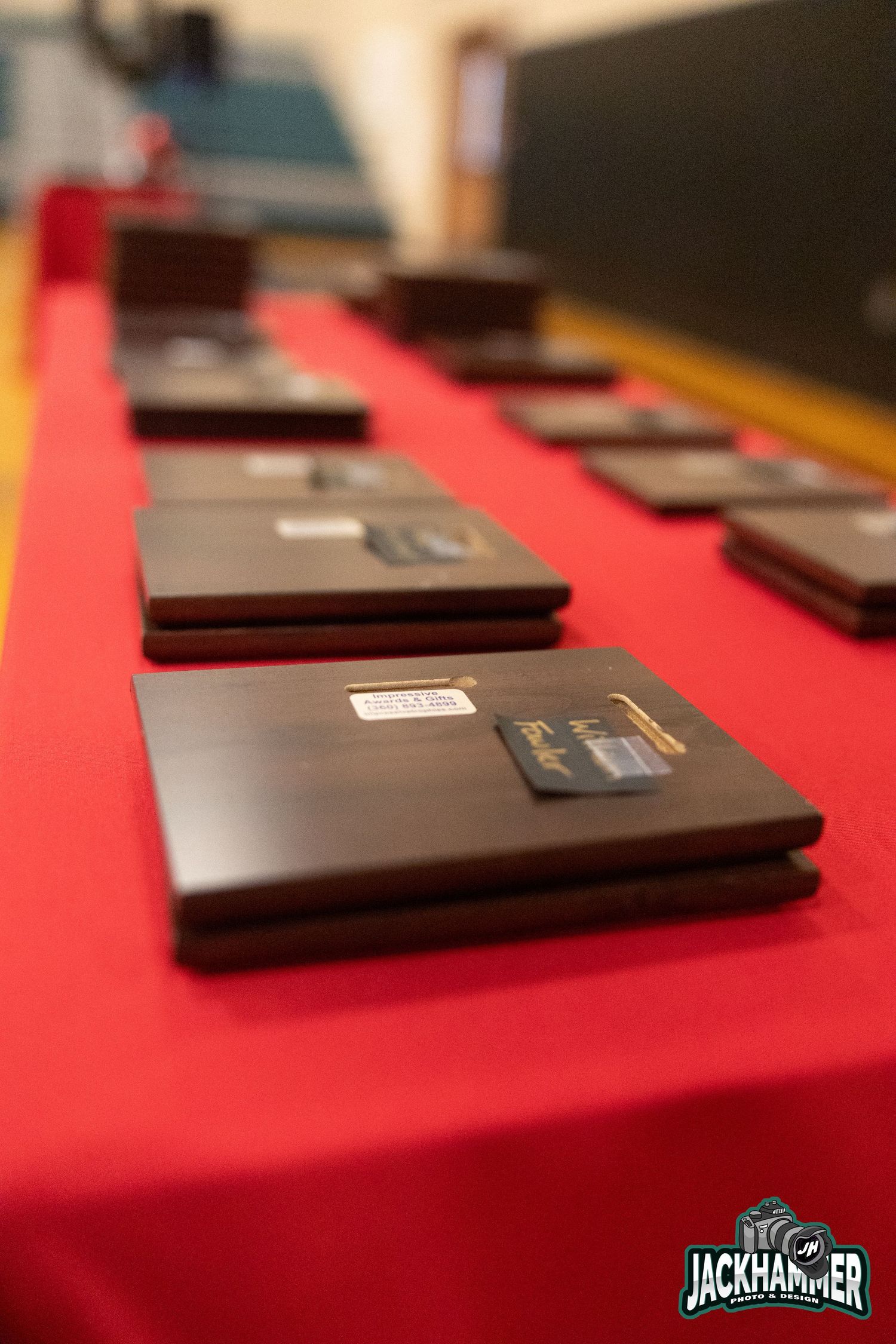 Dark wooden award plaques lined up on a red tablecloth at a Jackhammer ceremony.